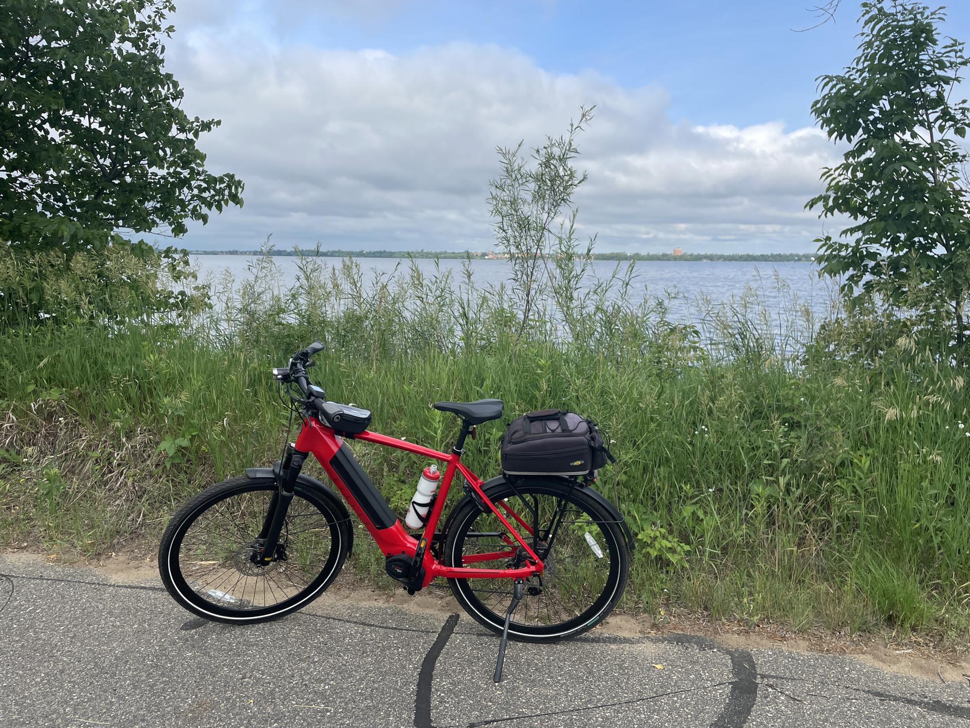 A red electric bicycle with a rear bag parked beside a lake.