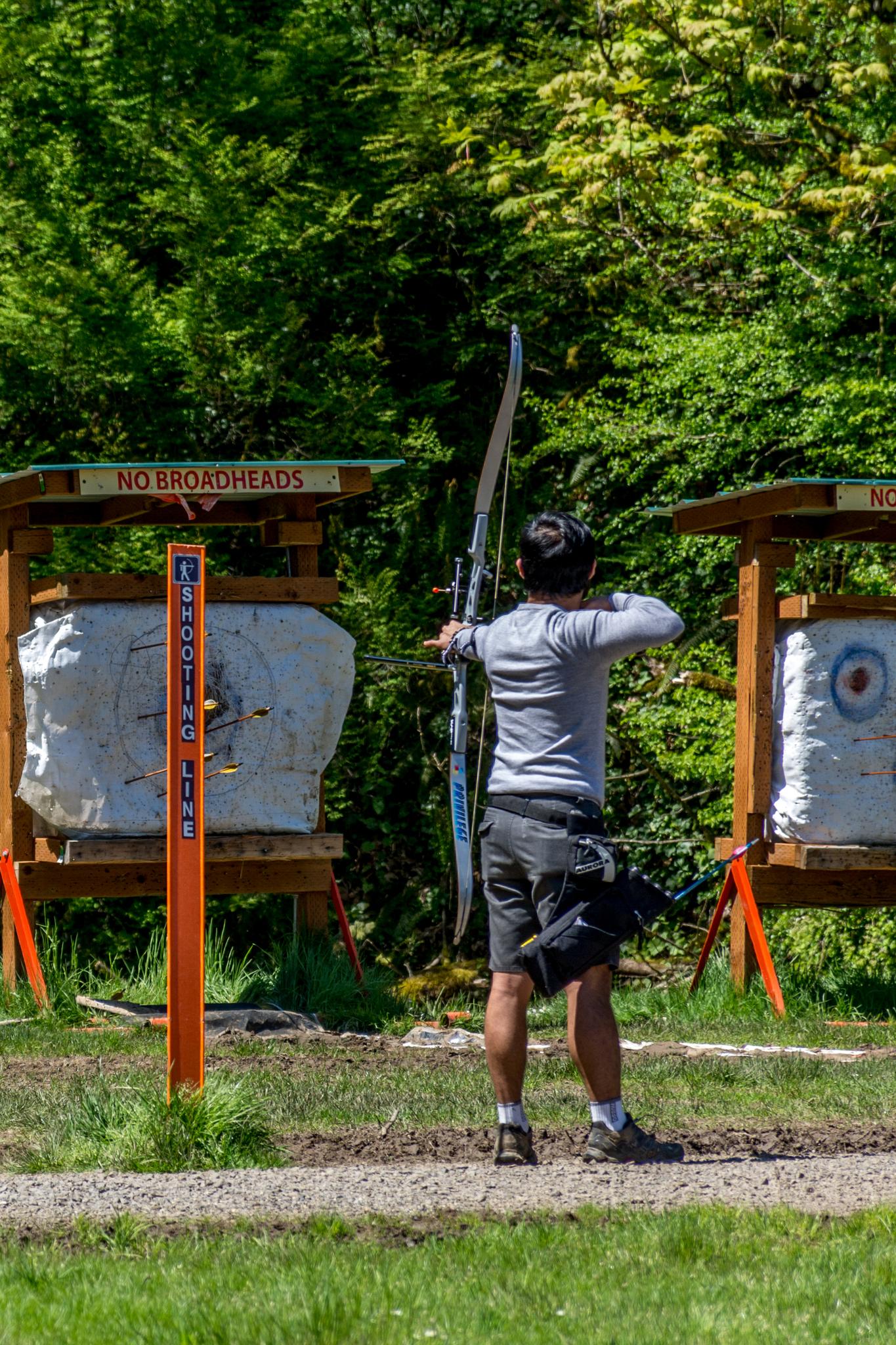 Person aiming a bow and arrow at targets on an outdoor archery range.