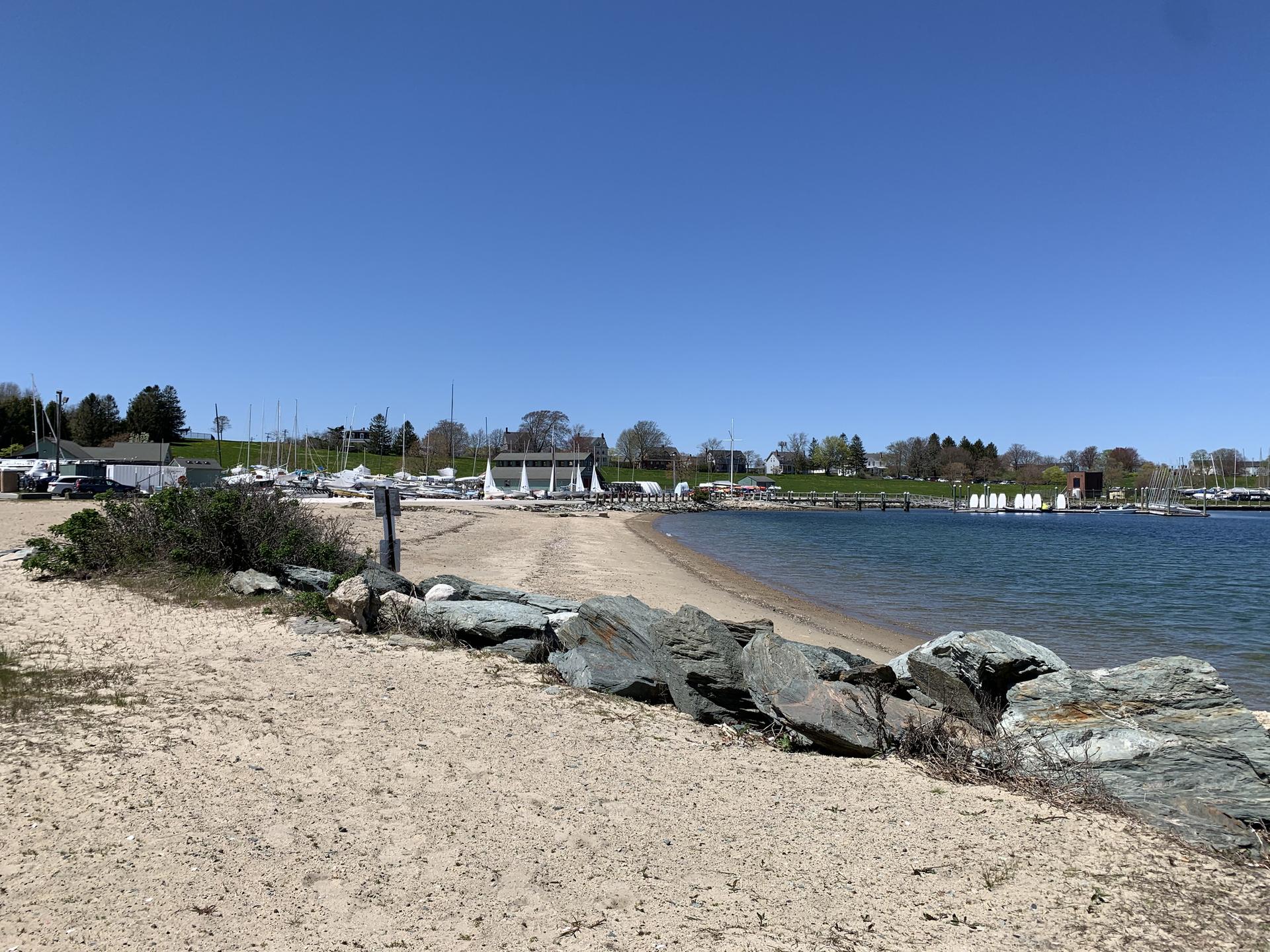 Sunny view of a sandy beach leading to a calm bay with a marina.