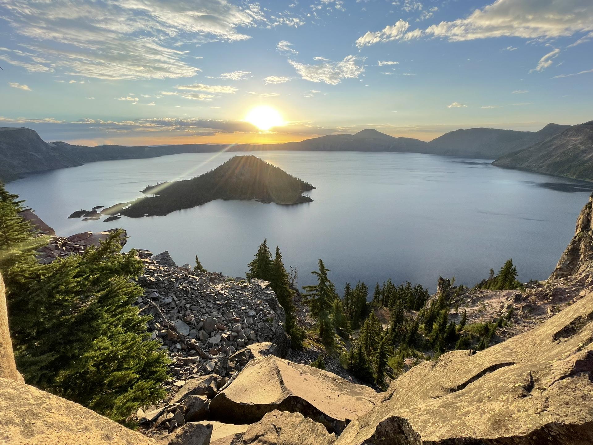 Sunset over a large lake with a central island, rocky foreground.