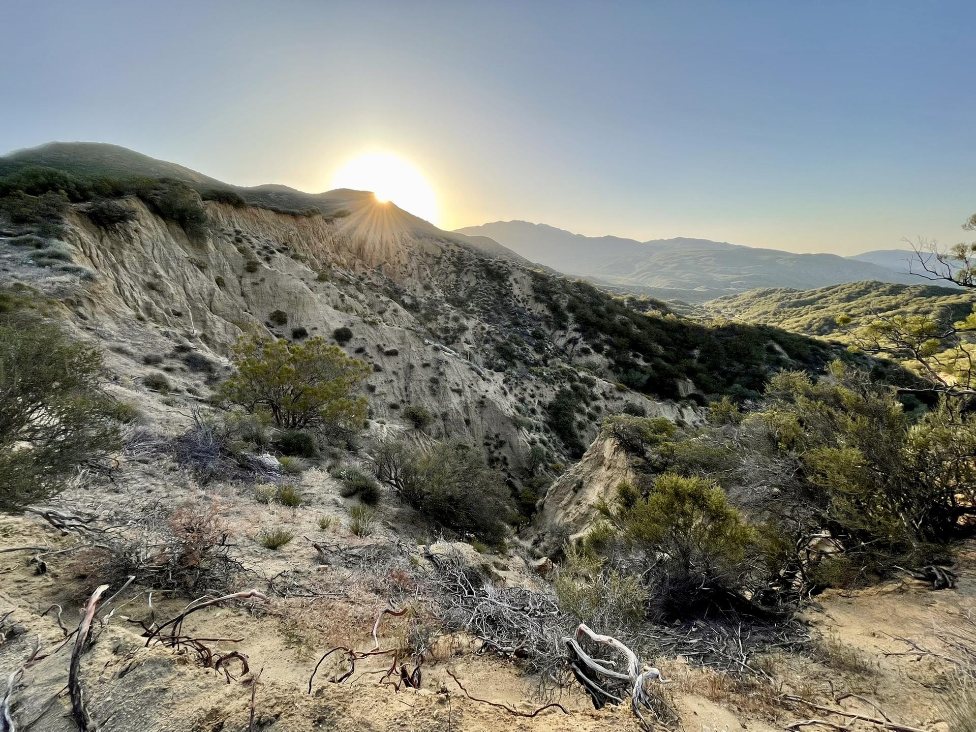 Sun setting over arid, eroded hillsides with scrub brush.