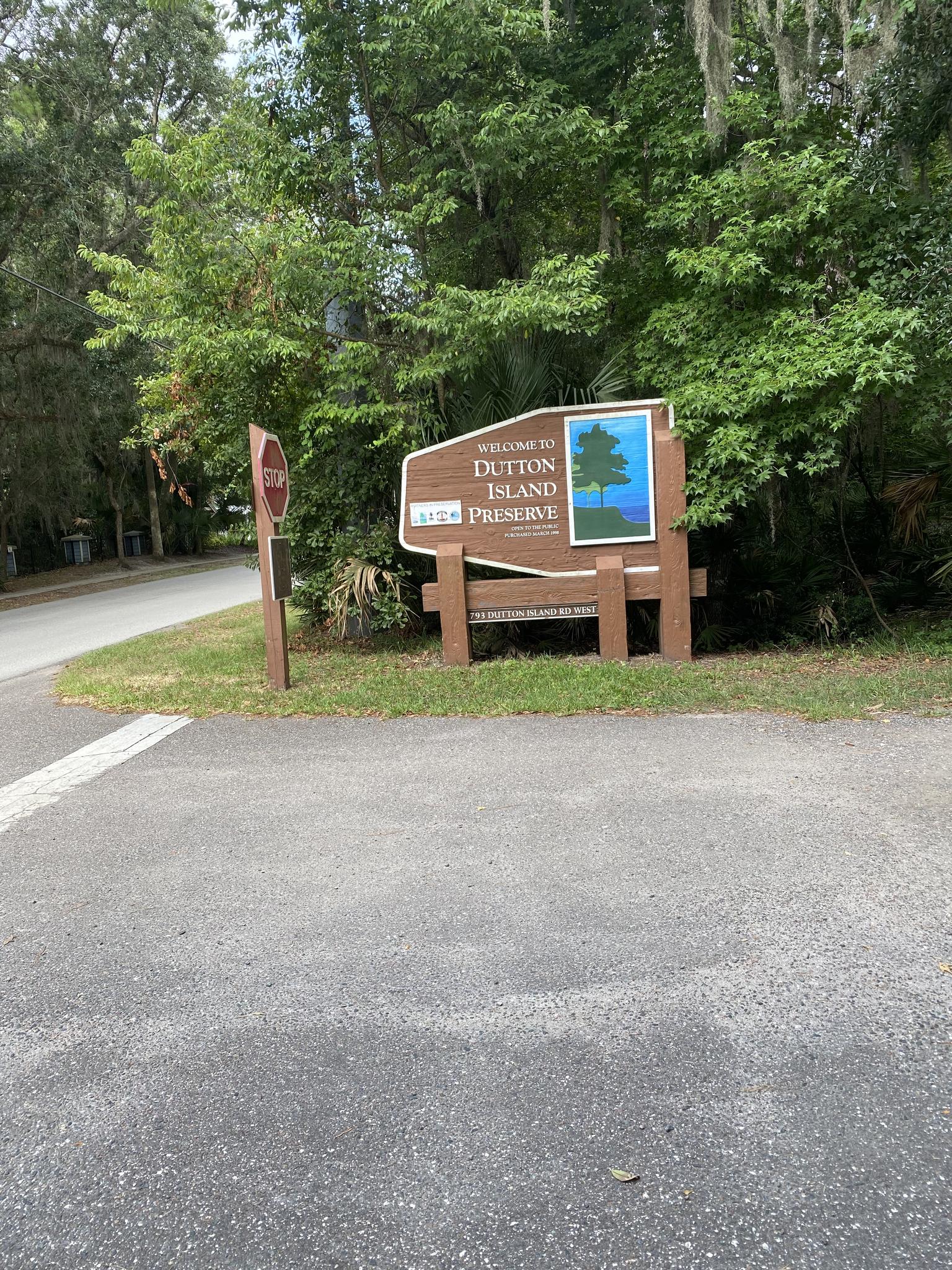 A large wooden sign stands by a road, surrounded by lush green trees.