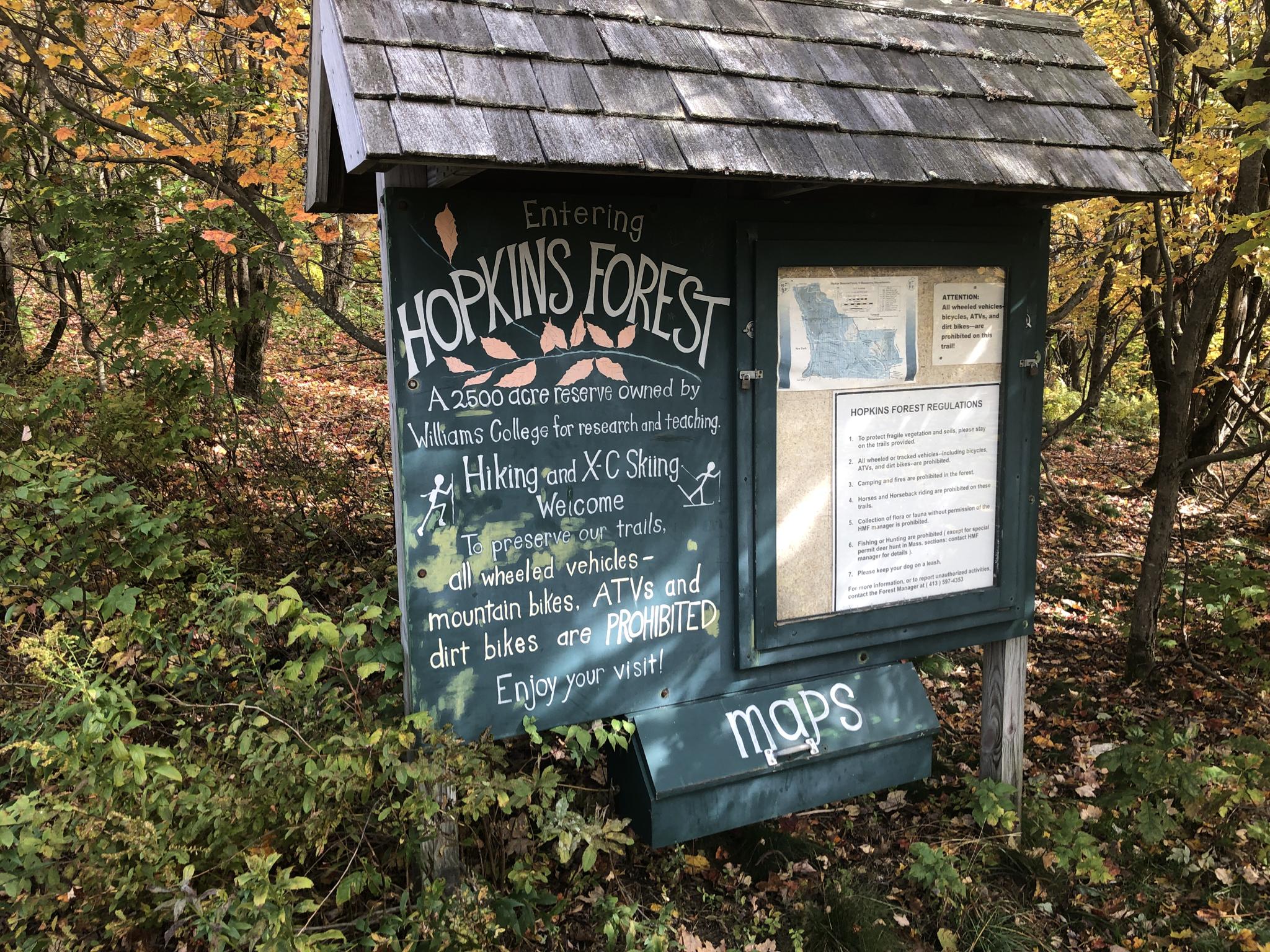Wooden trail sign with information, surrounded by autumn foliage.