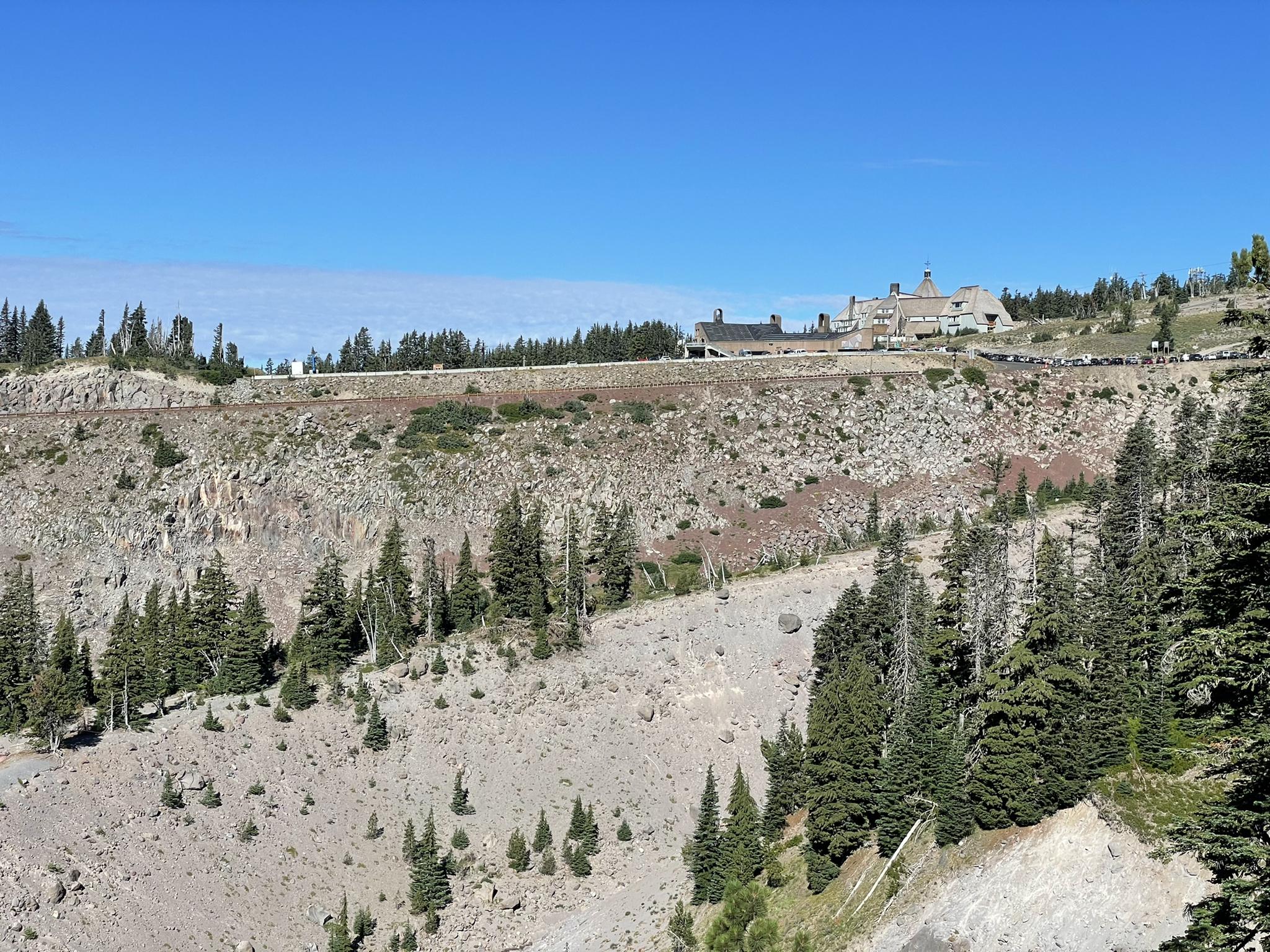Large building on a rocky, forested hillside under a clear blue sky.
