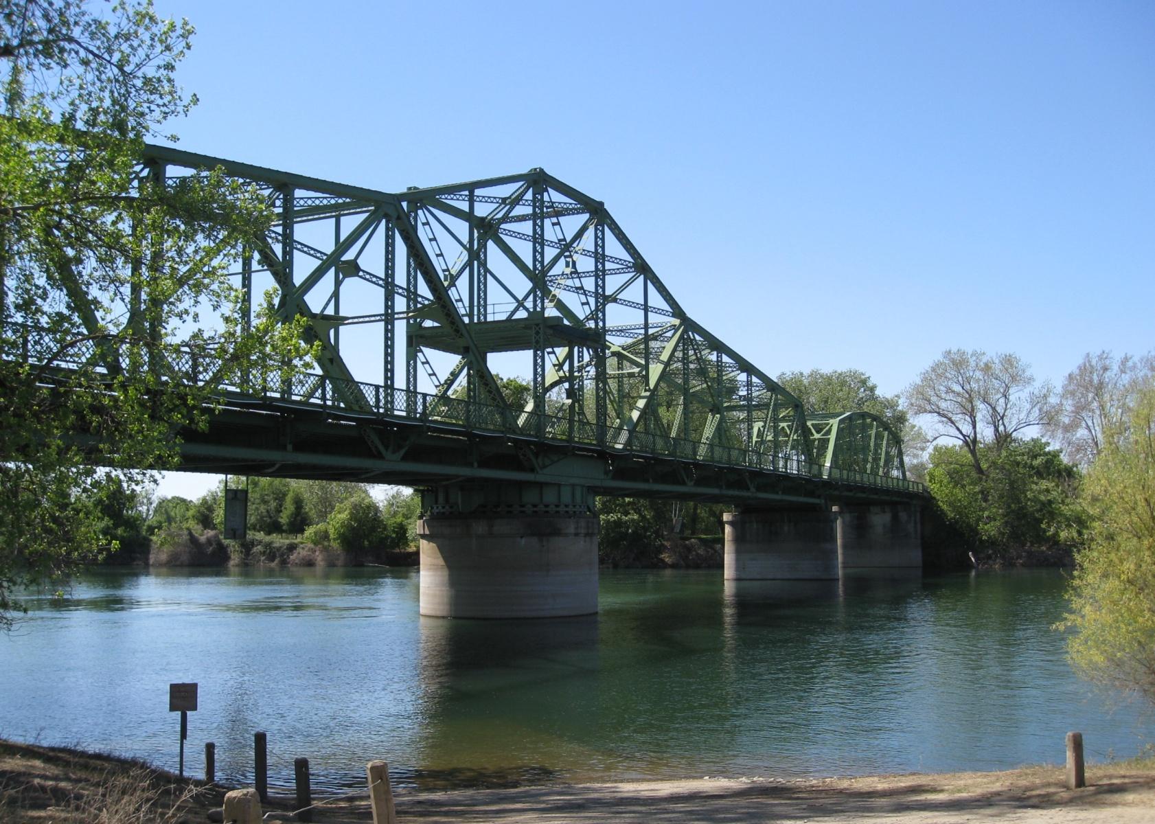 Green truss bridge spanning a wide river under a clear blue sky.
