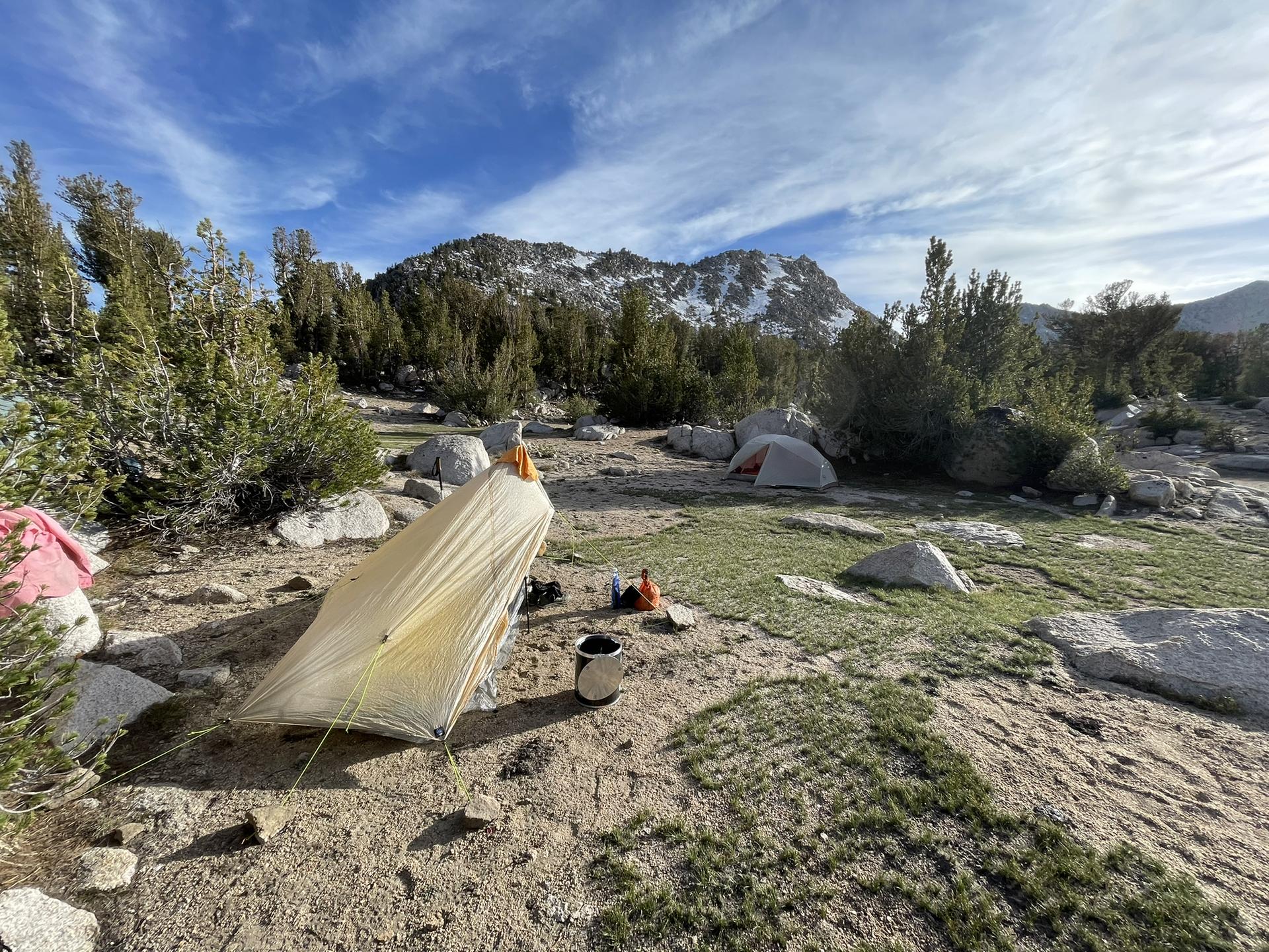 Two tents are set up in a rocky, open campsite under a blue sky.