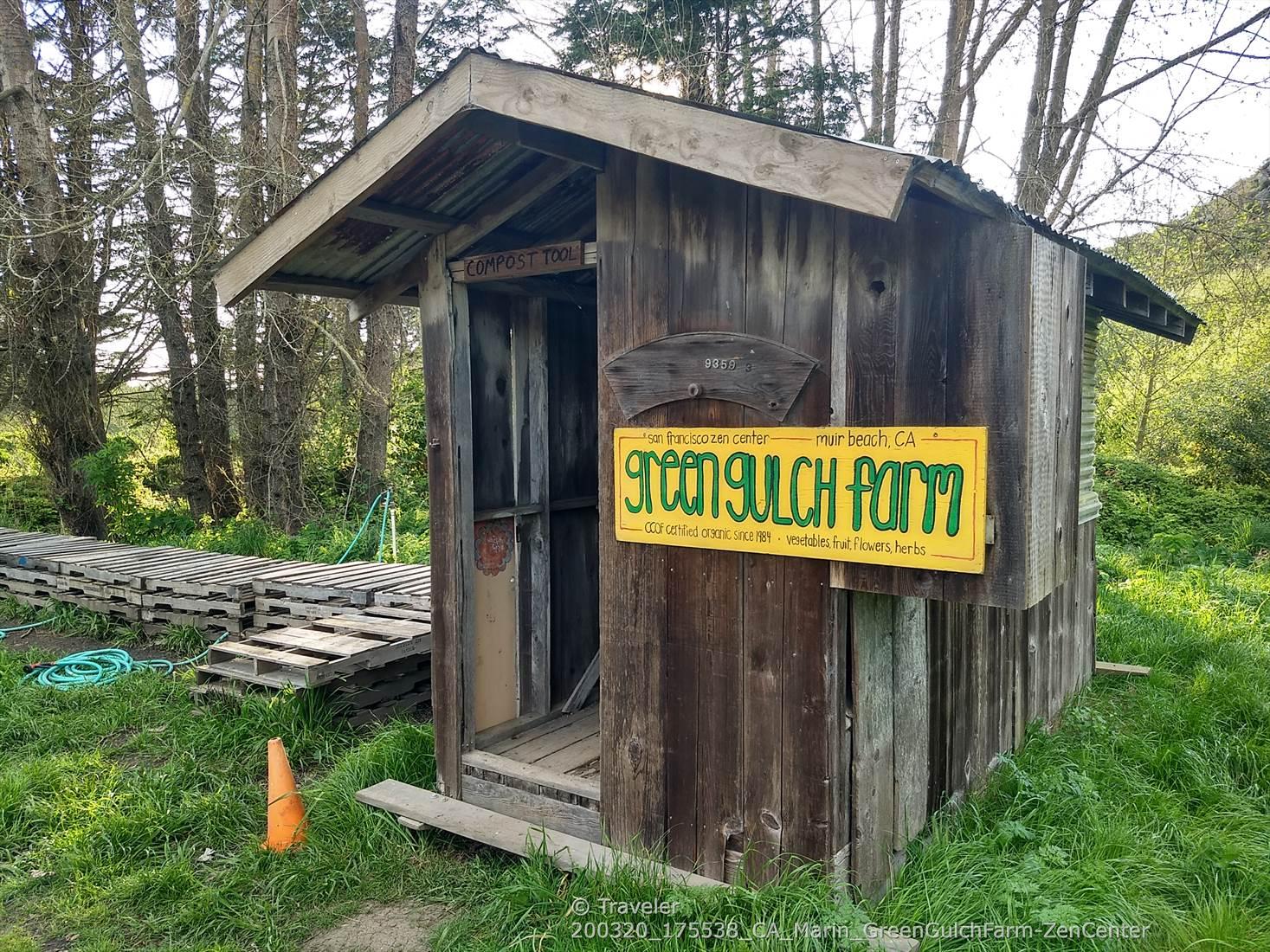 A rustic wooden shed with a yellow sign stands in a grassy, wooded area.
