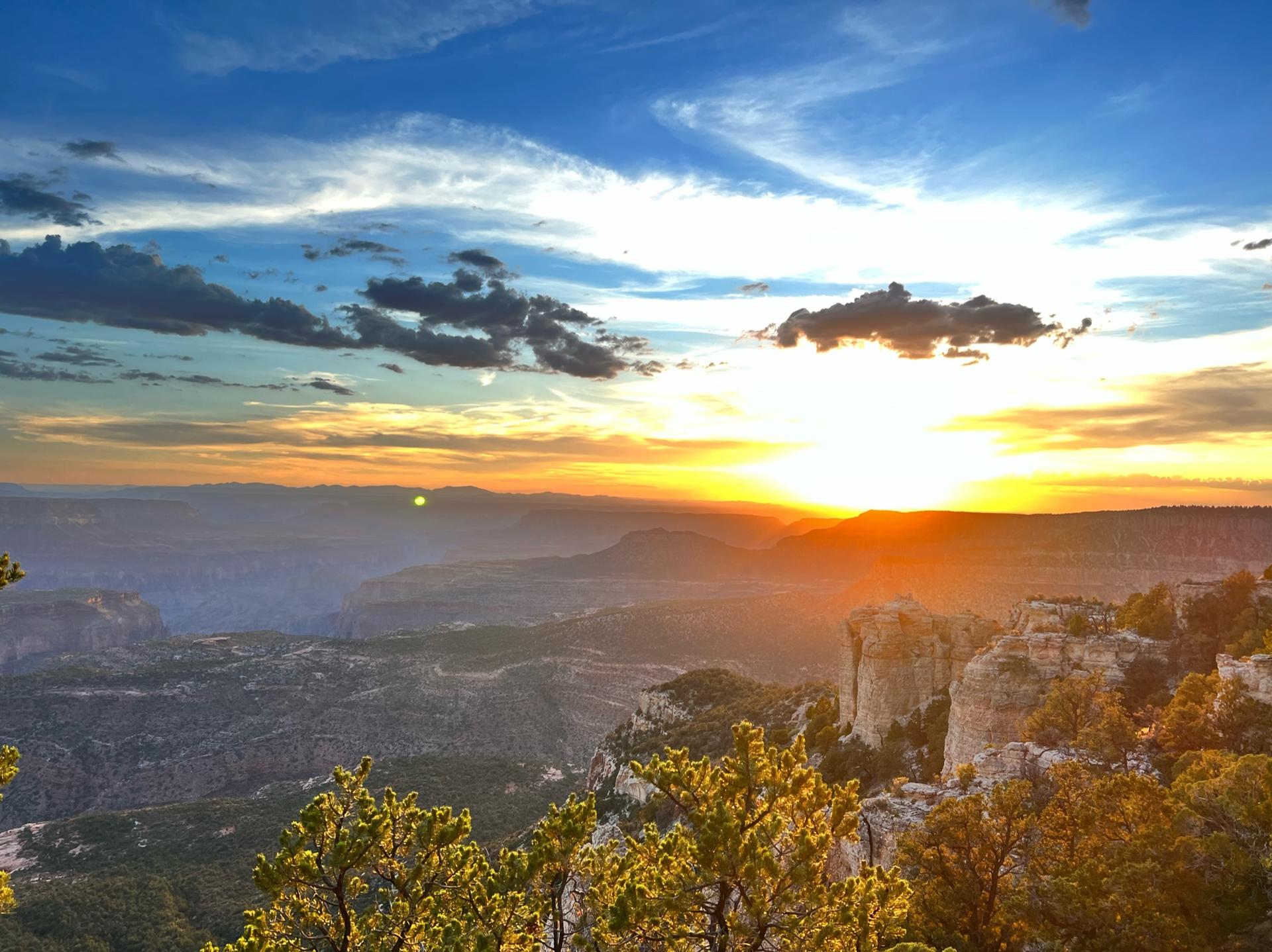 Dramatic sunset over a vast, rugged canyon landscape with golden light.
