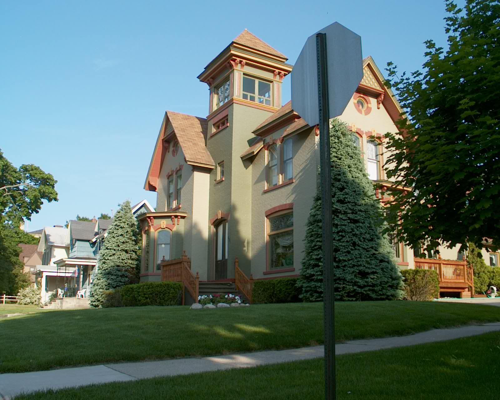 A large, ornate house with a tower, green lawn, and clear sunny sky.