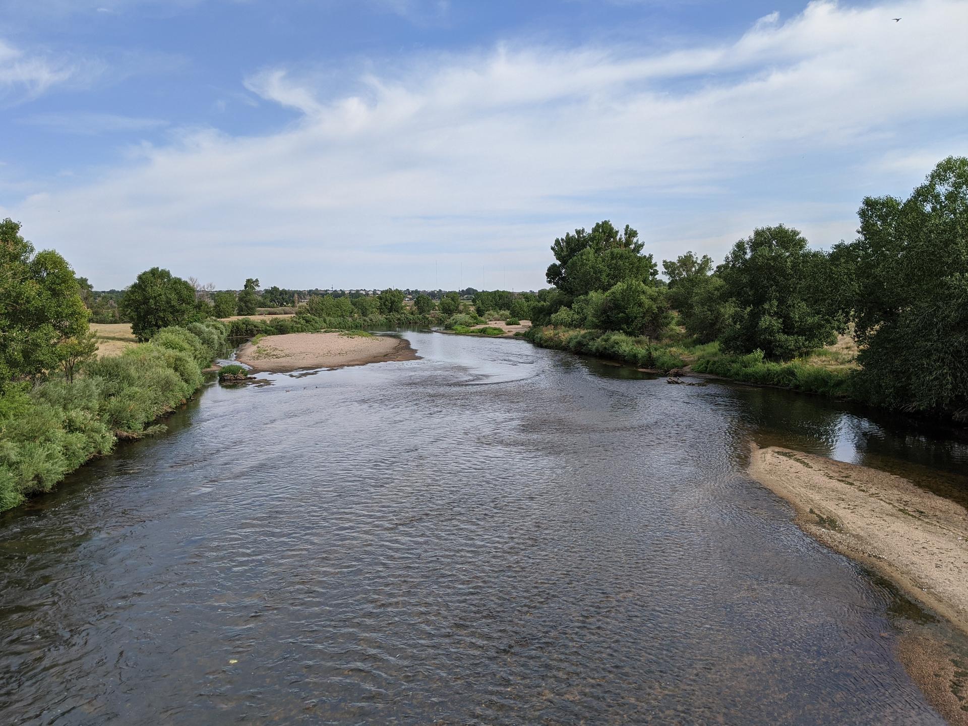 Wide river flowing between green banks under a bright, cloudy sky.