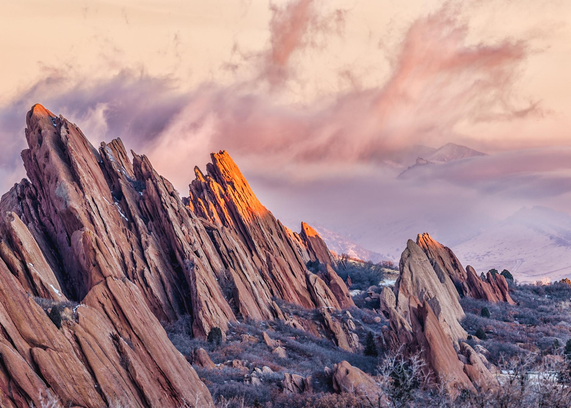 Dramatic red rock formations glowing at sunset under pink and purple clouds.