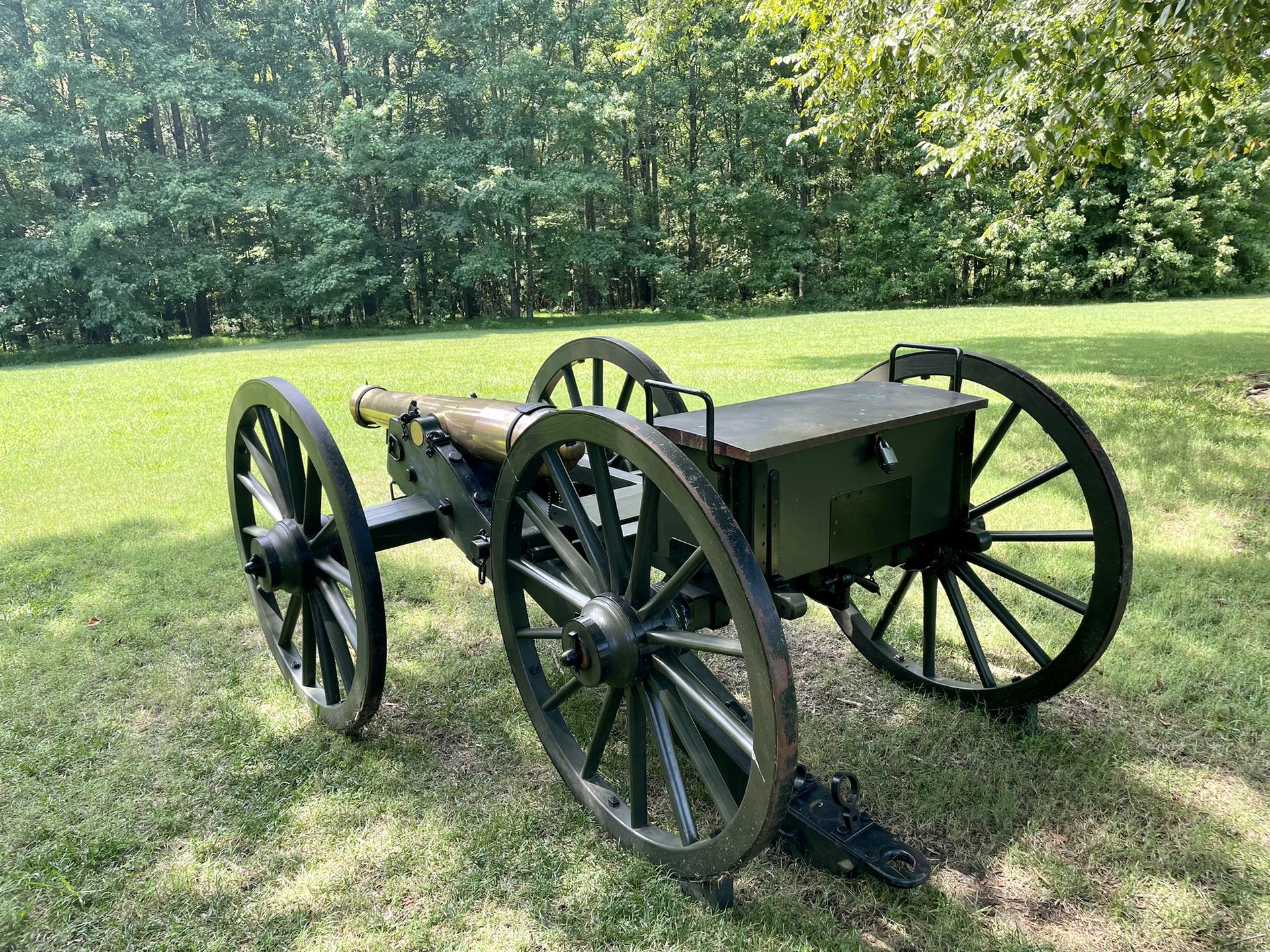 An old cannon and caisson on a sunny grassy field with trees.
