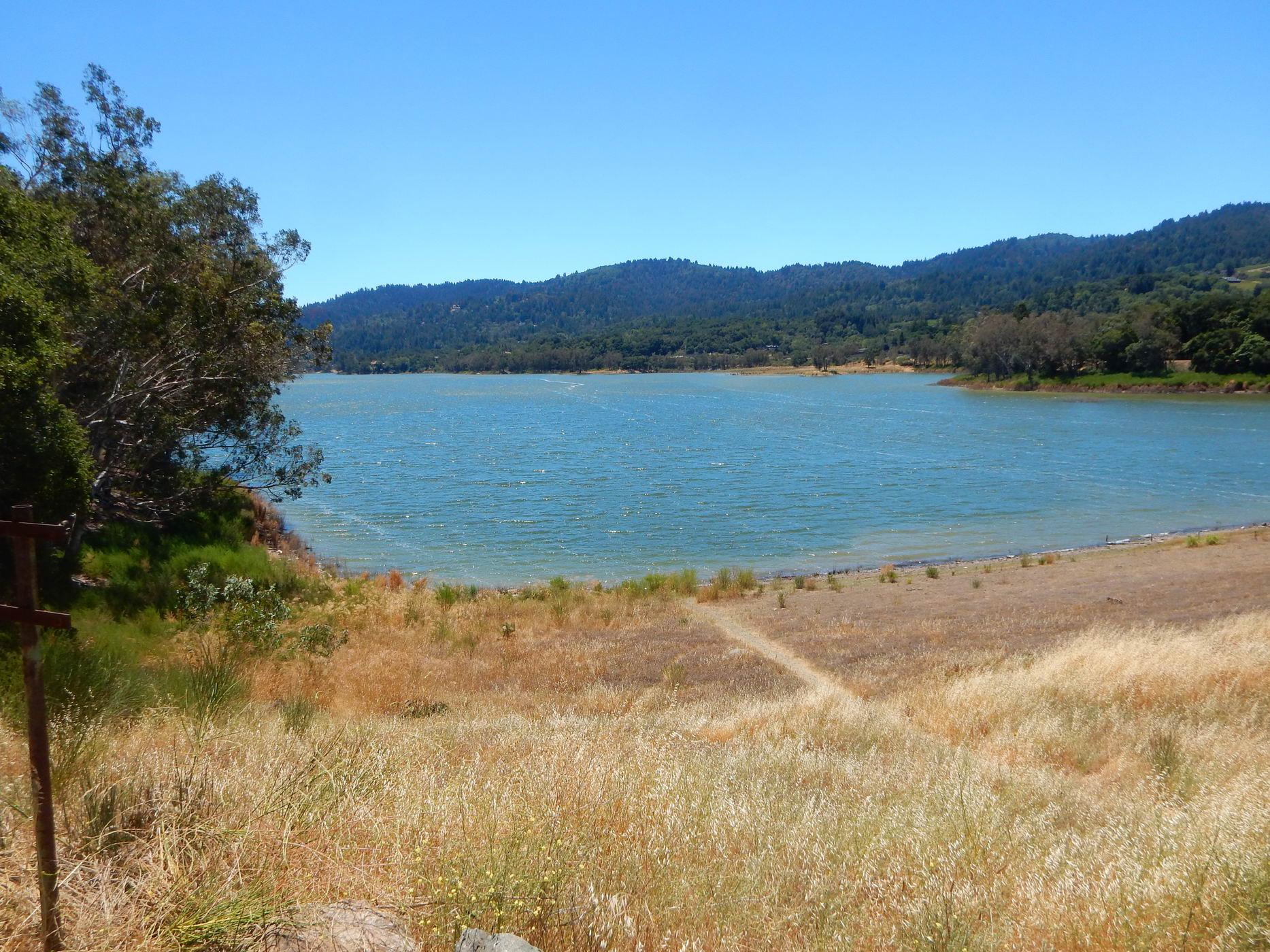 A wide view of a blue lake surrounded by green hills and dry grass.