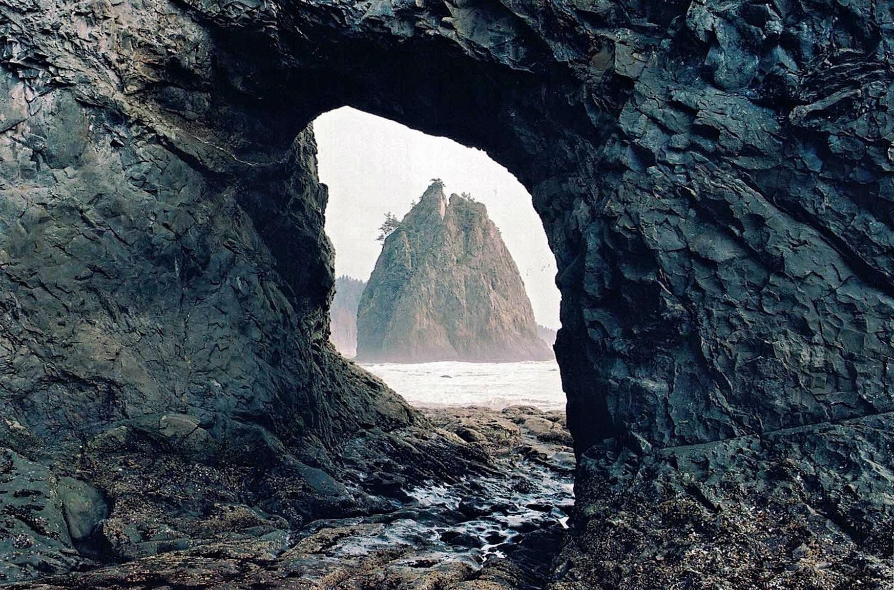 Sea stack framed by a dark rock arch on a misty day.