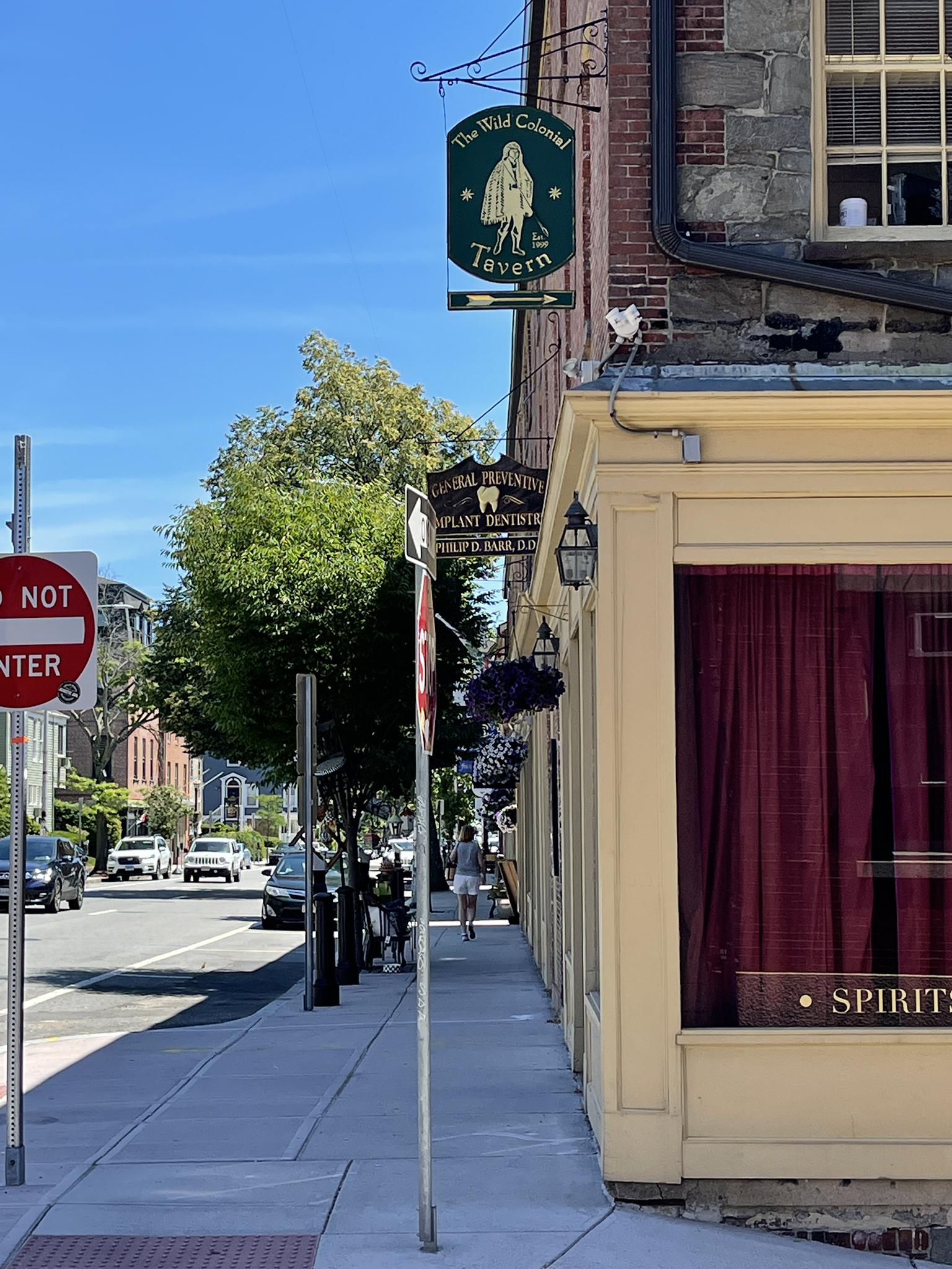 Historic building with a tavern sign, a sunny street, and a distant pedestrian.