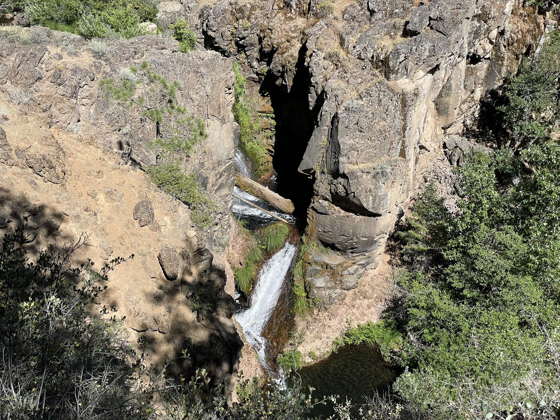 A waterfall cascades down rugged, mossy rock cliffs into a shaded pool.