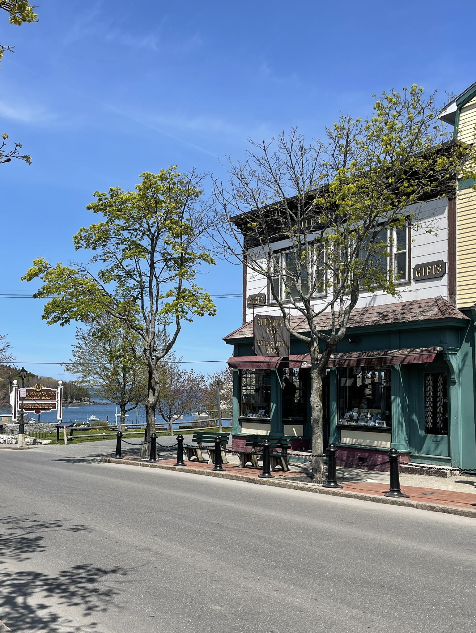 Sunny street scene with a building, trees, and water in the background.