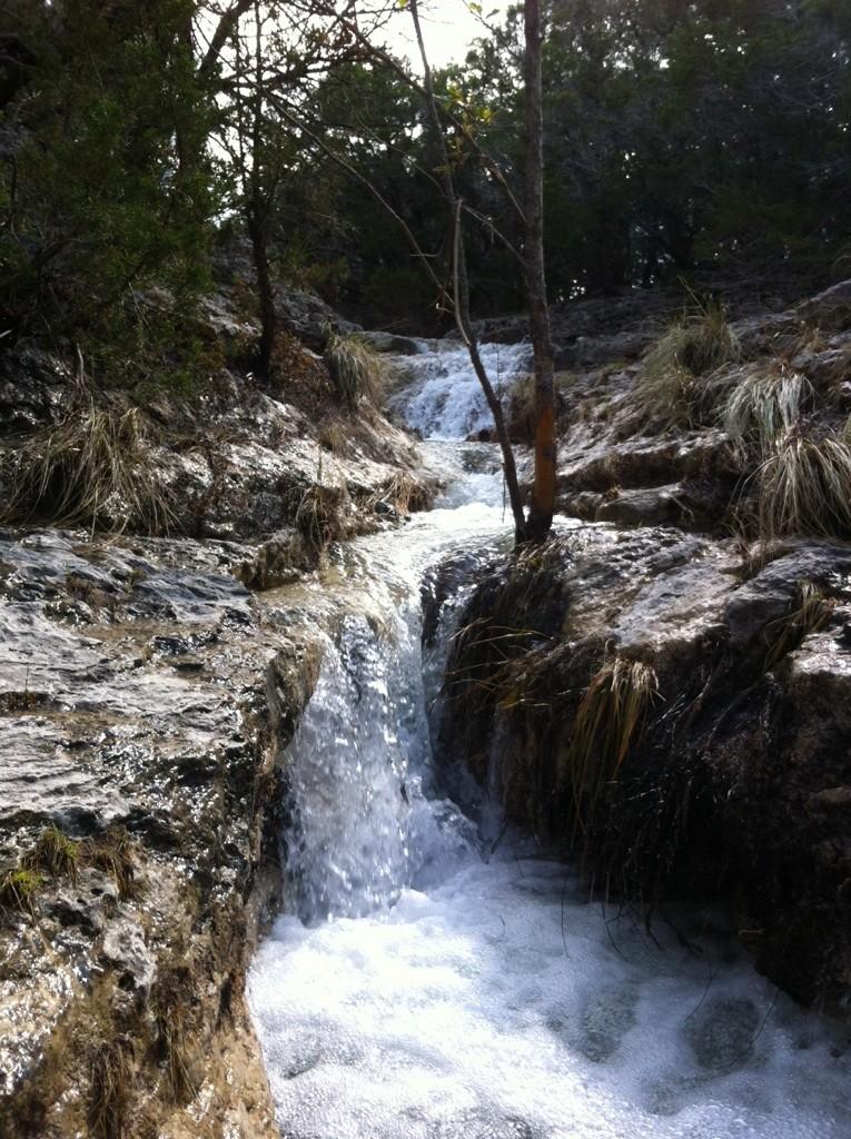 A small waterfall cascades over rocky terrain with sparse trees and grass.