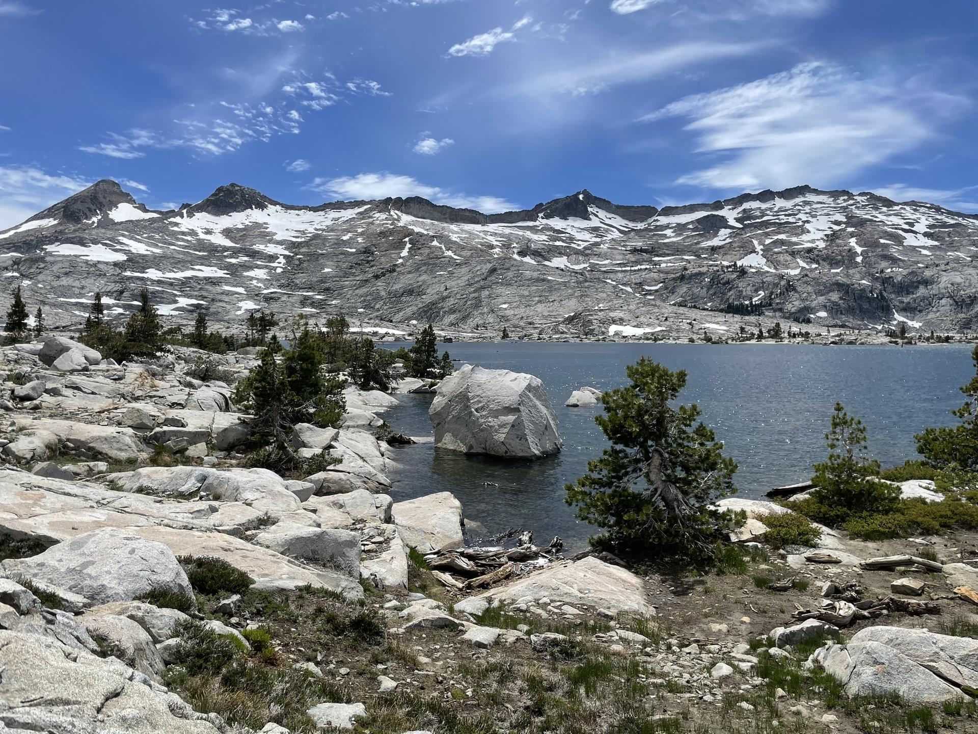 Rocky shoreline with a large boulder in the lake, snowy mountains in the background.