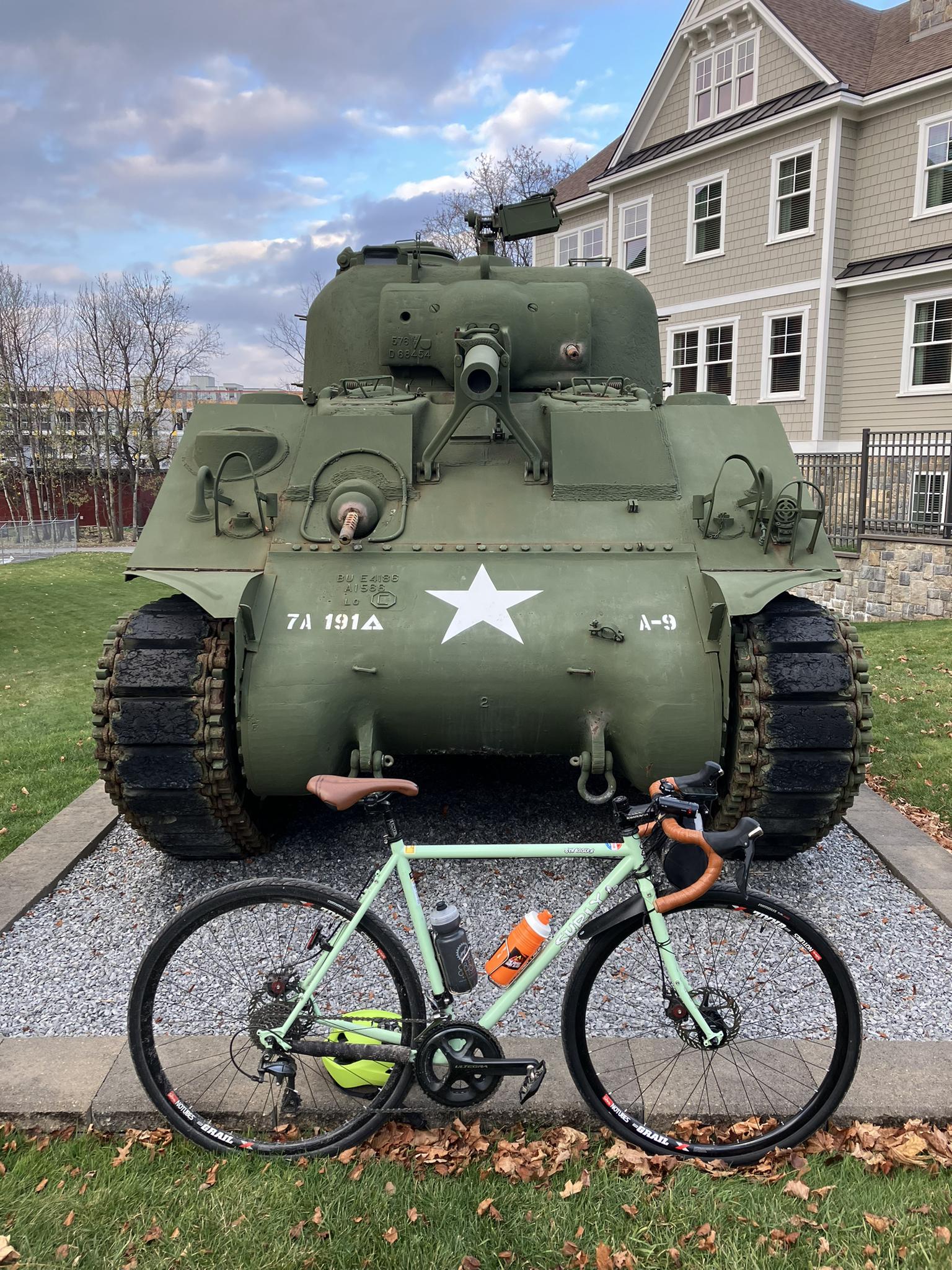 A light green bicycle parked in front of a large green military tank.