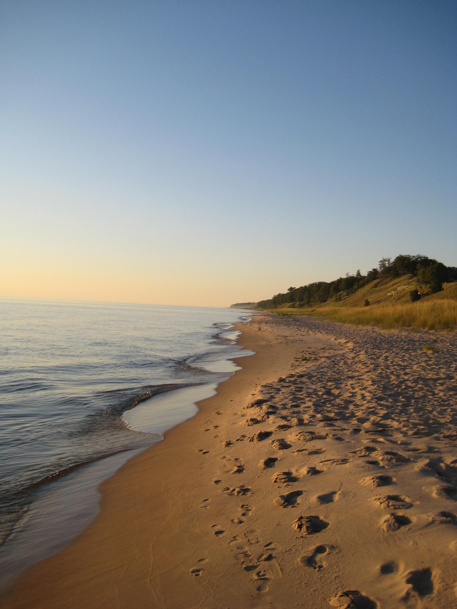 Golden hour light on a sandy beach with waves and footprints.