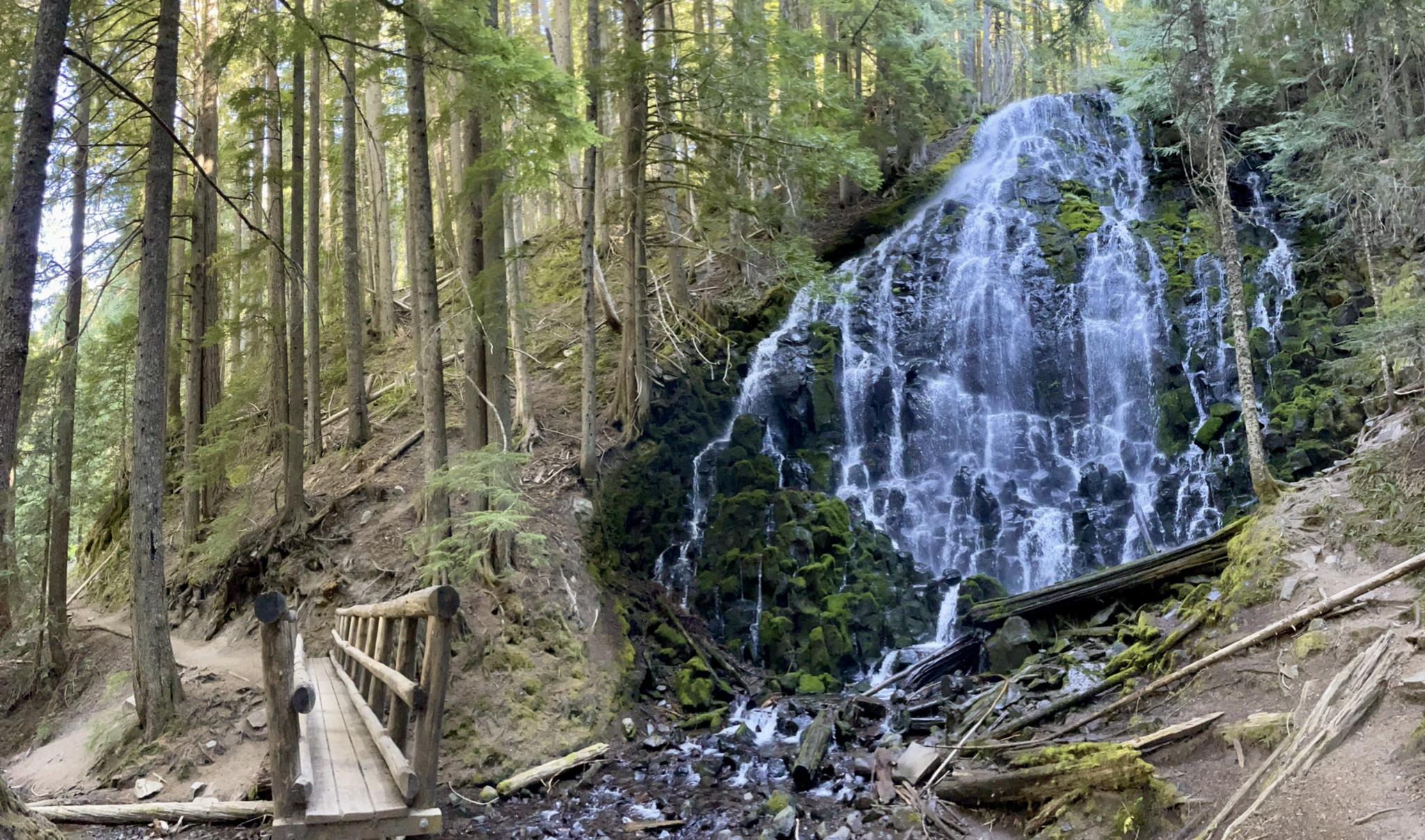 Large waterfall cascading over mossy rocks next to a wooden bridge.