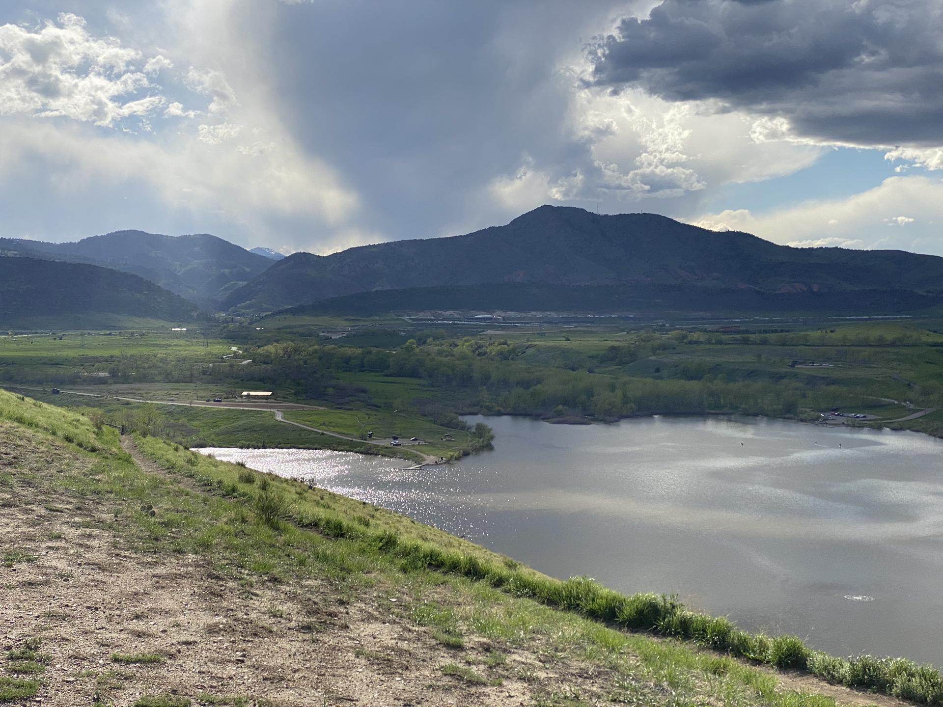 Overcast sky above a large lake, green hills, and distant mountains.