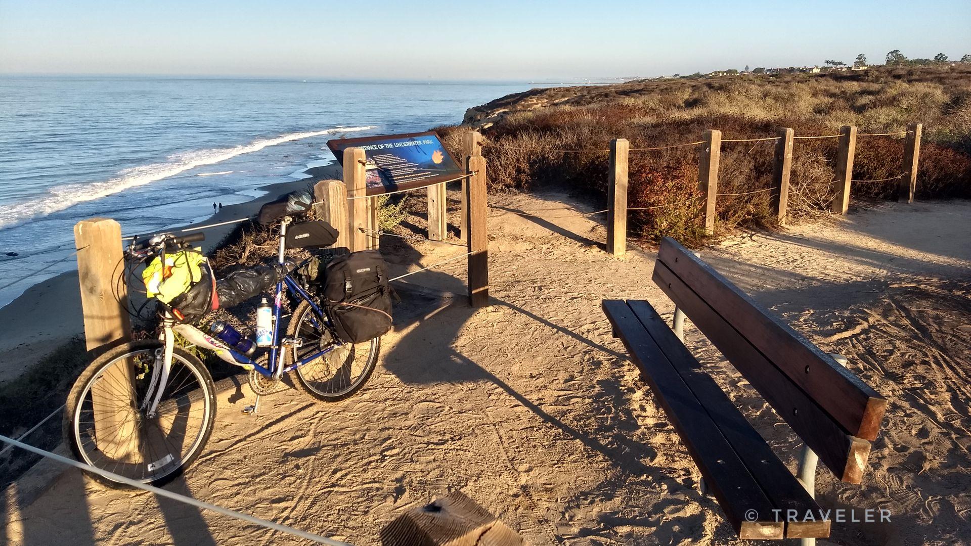 Bicycle parked on a sandy bluff overlooking the ocean at sunset.