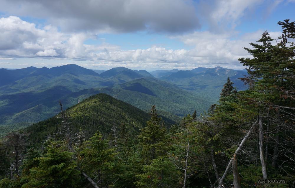 Lush green mountains stretch under a partly cloudy sky, with evergreen trees.