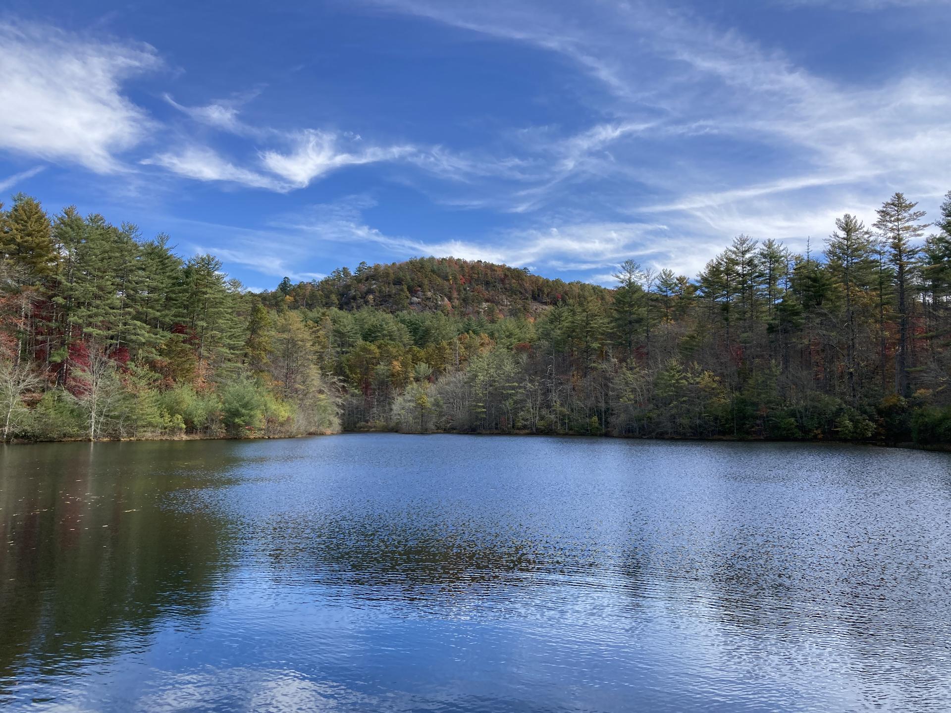 Calm lake reflecting blue sky and colorful autumn trees under bright sun.