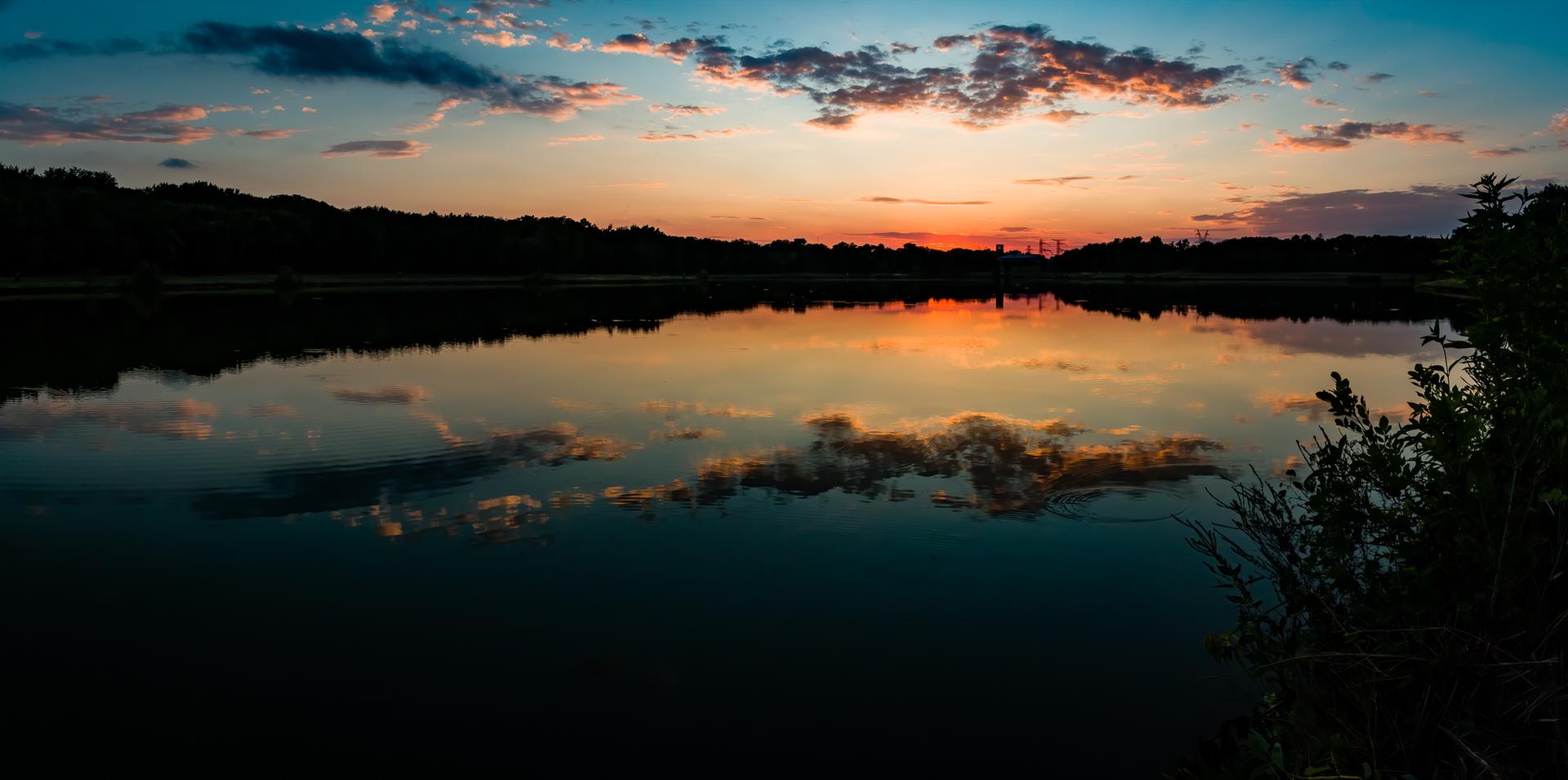 A vibrant sunset over a calm lake, reflecting colorful clouds beautifully.