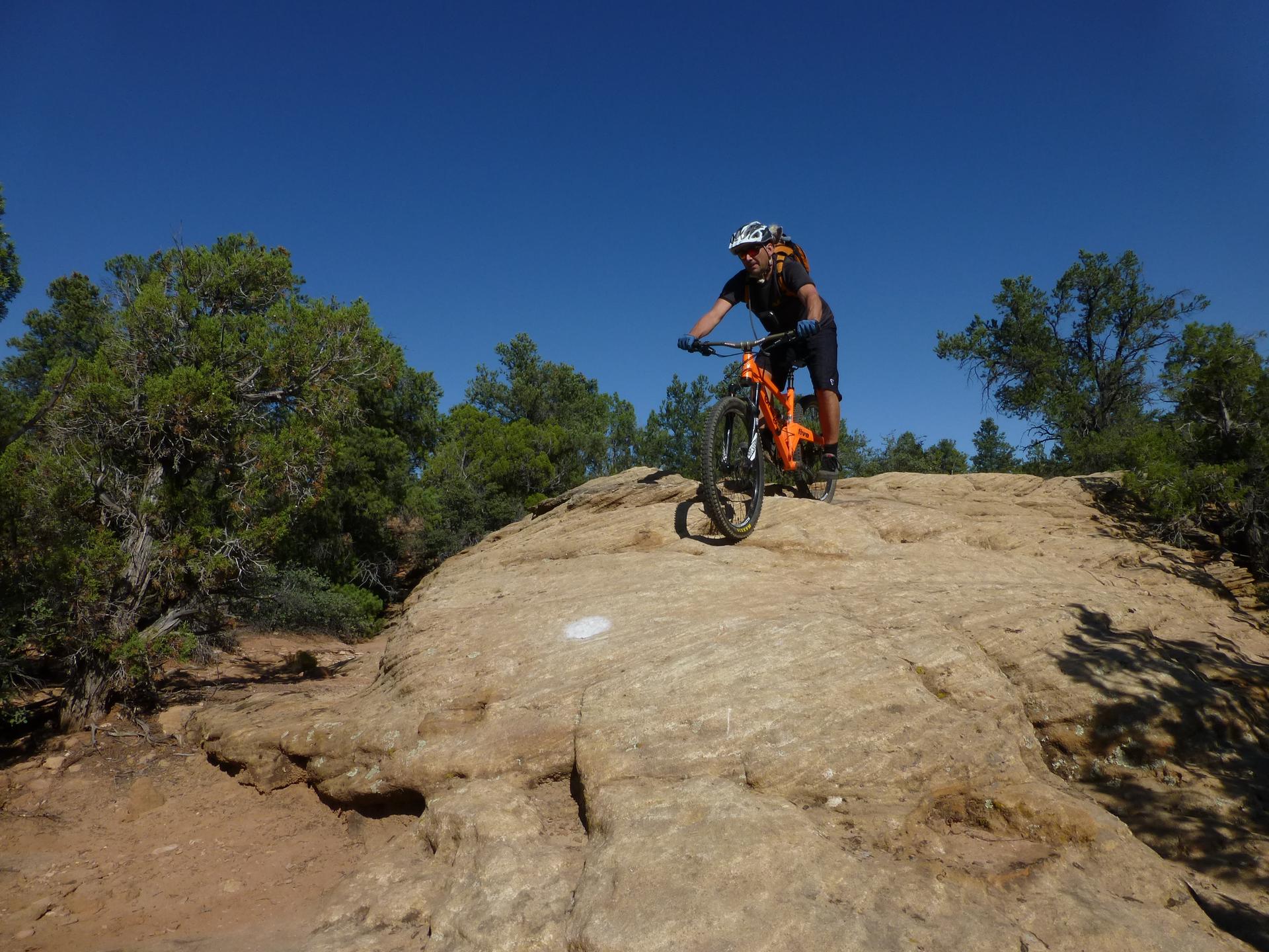 A person on an orange mountain bike riding up a rocky outcrop.