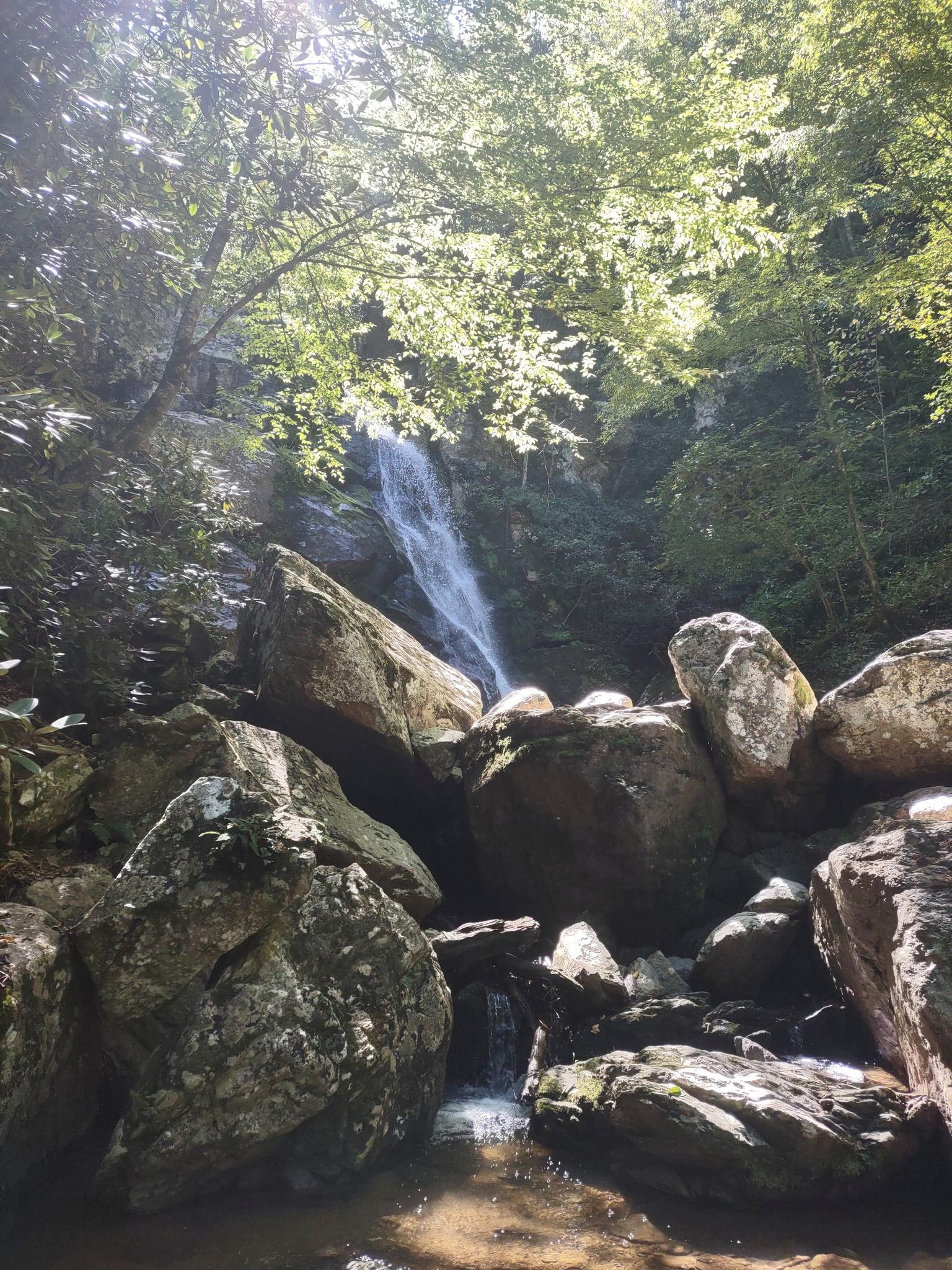 Tall waterfall cascading into a rocky pool under bright sunlight.