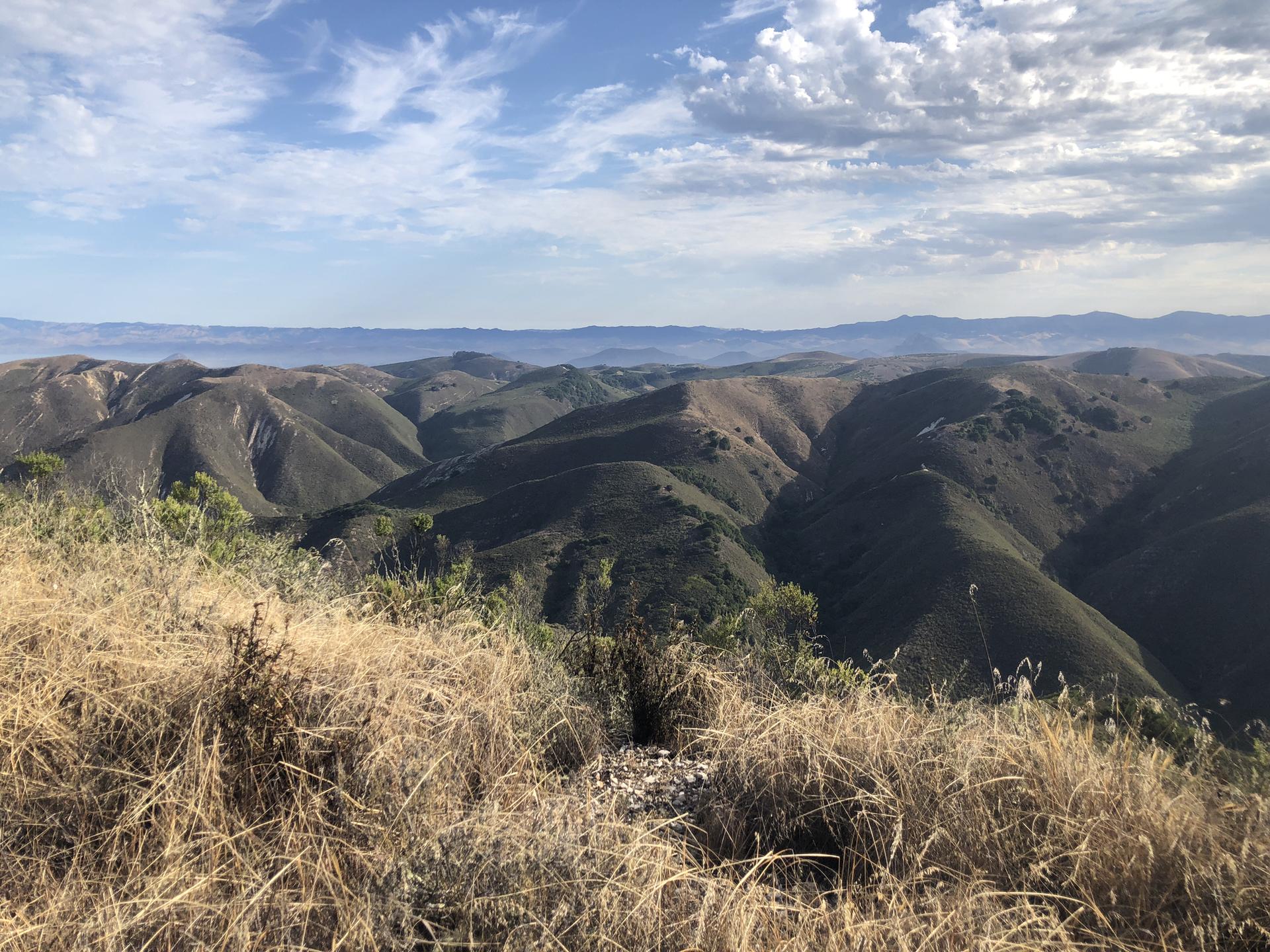 Expansive view of dry, rolling hills under a partly cloudy sky.