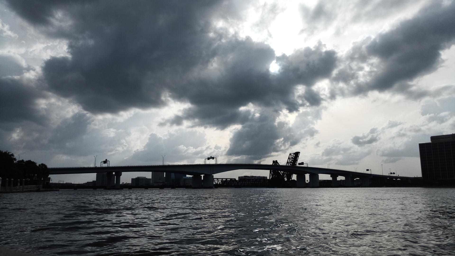 Dark silhouette of a bridge over water under heavy, stormy clouds.