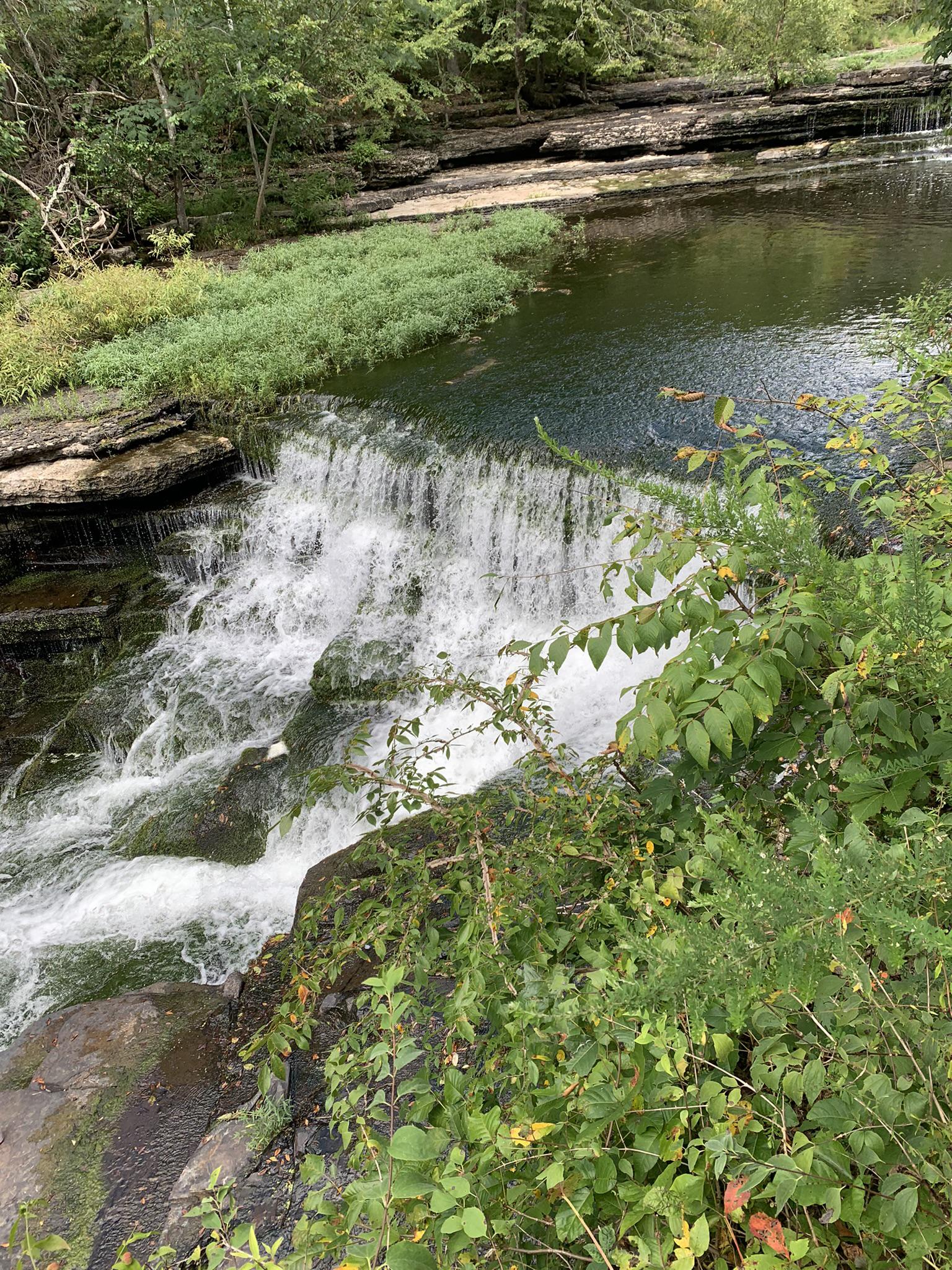 A multi-tiered waterfall cascades over rocks, surrounded by green foliage.