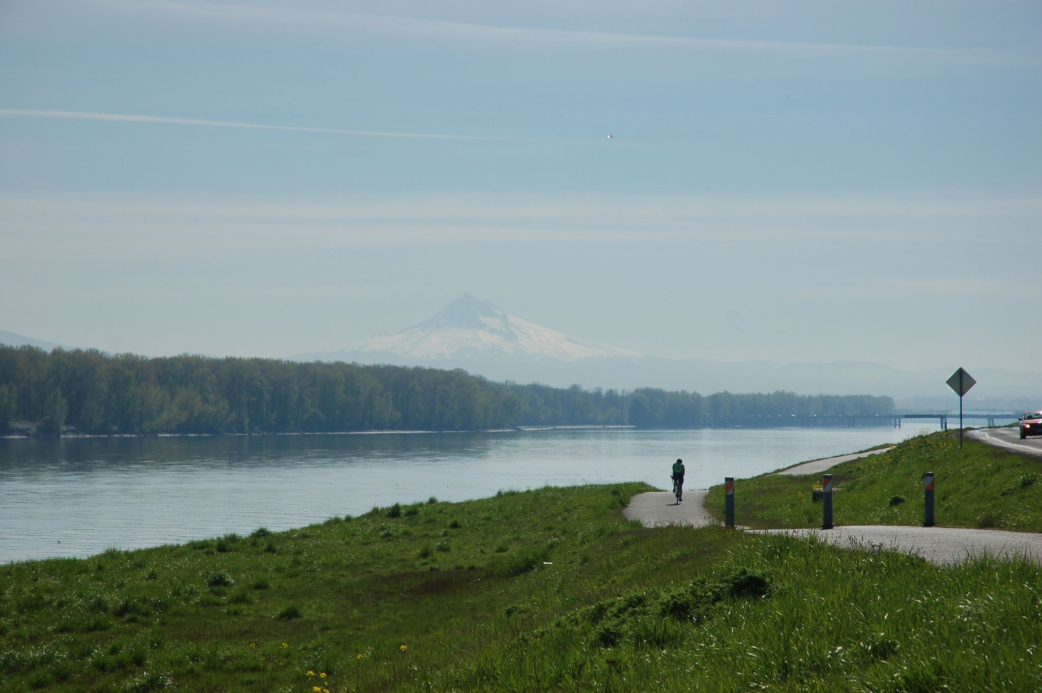 Person walks on a paved path beside a wide river and forested bank. - Historic Columbia River Highway and Marine Drive Loop