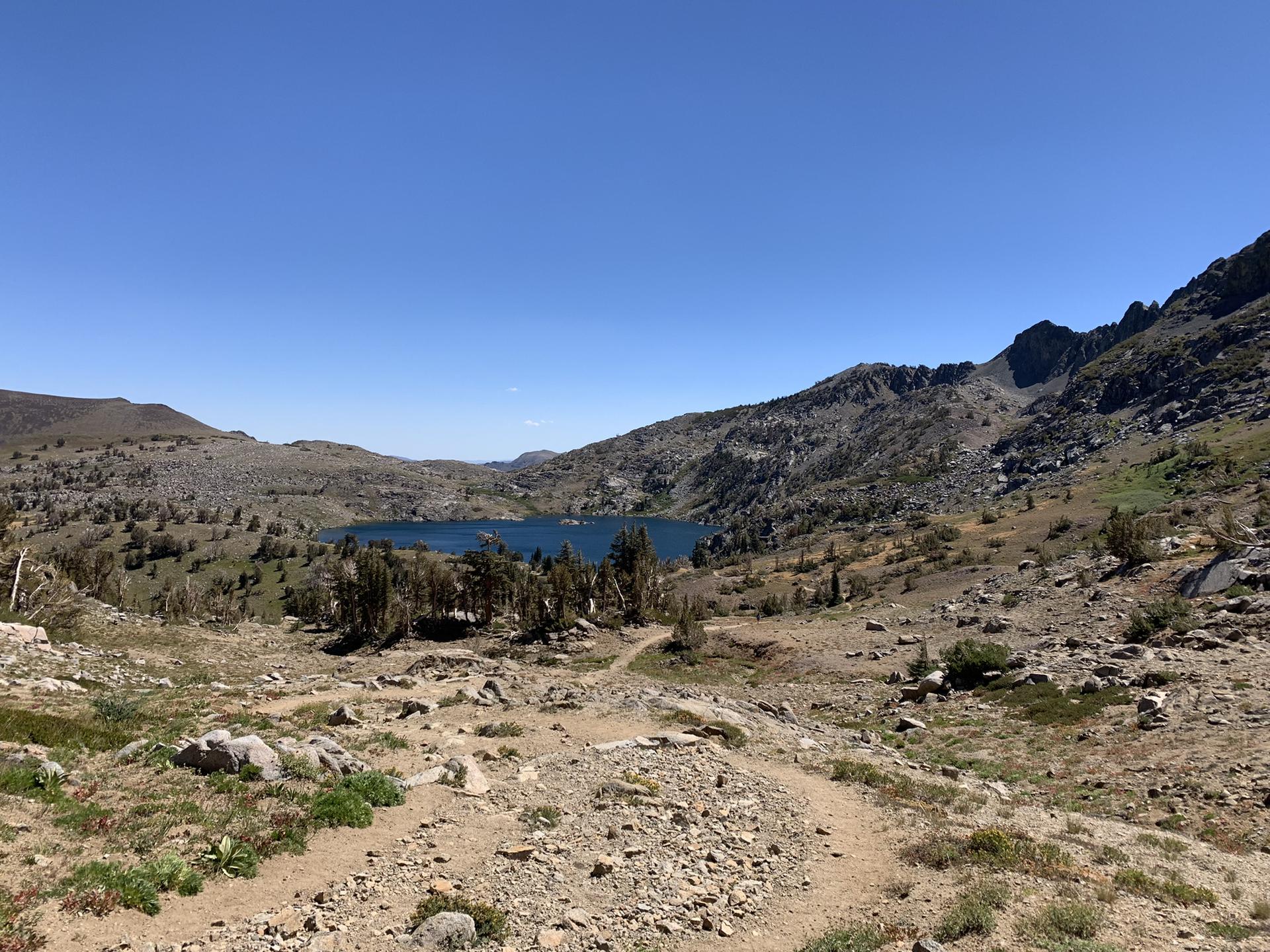 Sunny view of a blue mountain lake surrounded by rocky, arid terrain.