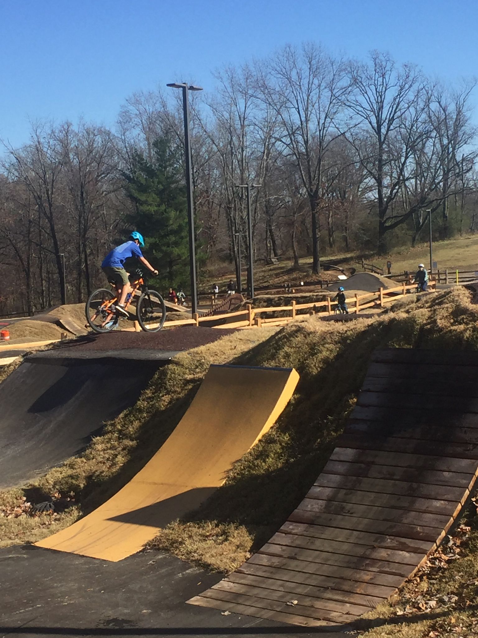 Person on a bike at a sunny outdoor bike park with ramps and trees. - Railyard Bike Park – Downtown Rogers loop from SE J St at Haas Hall (Northbound)