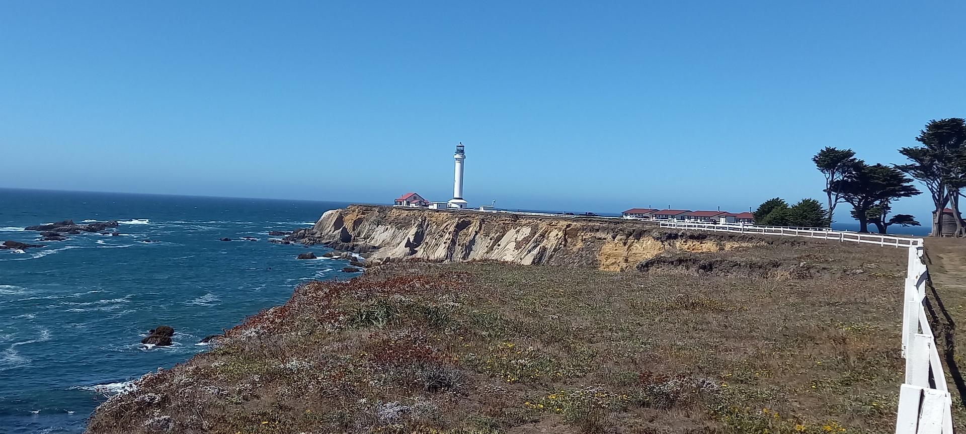 Panoramic view of a lighthouse on a grassy cliff overlooking the vast ocean.