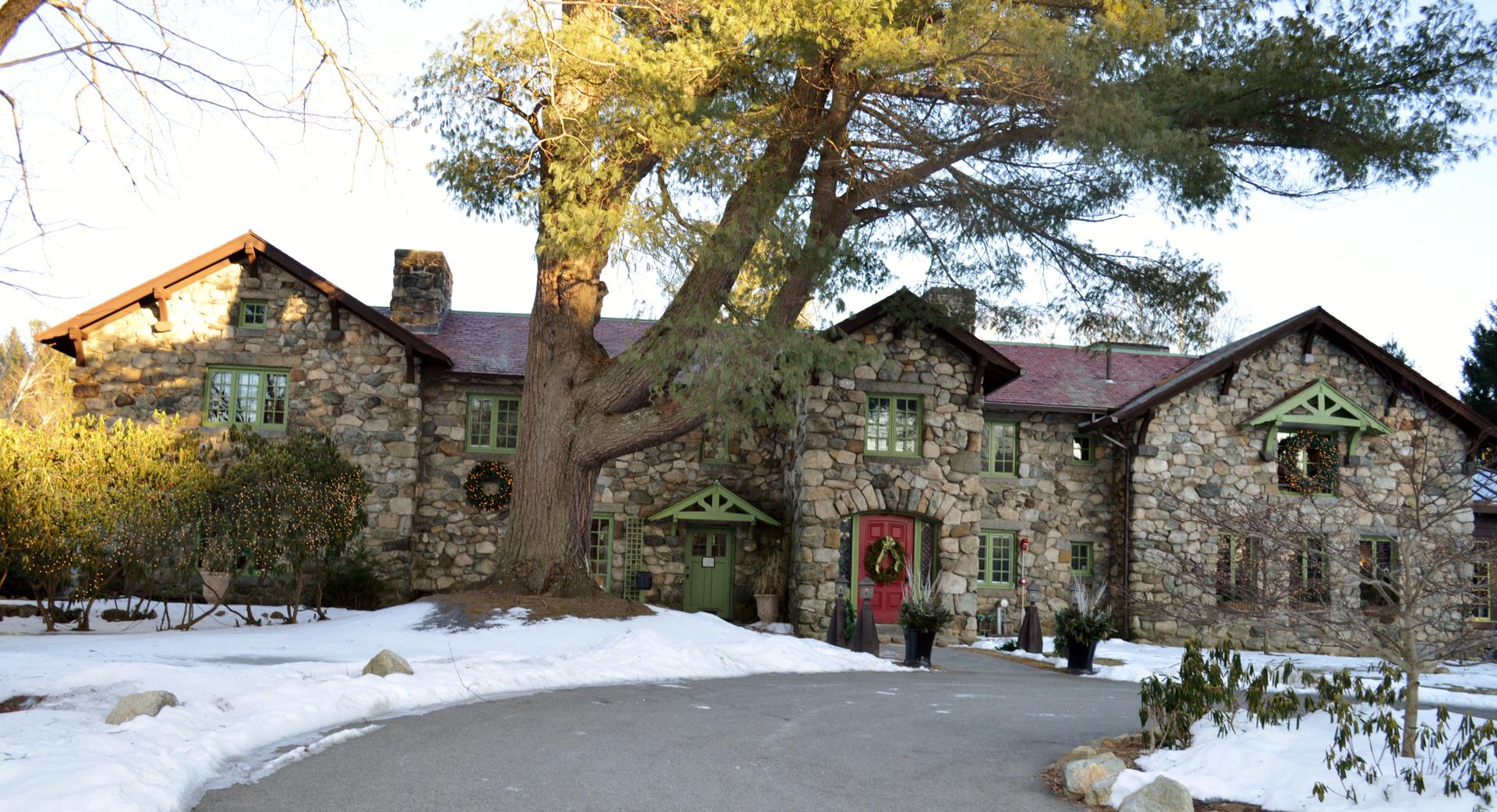 Large stone house with a huge tree in front, surrounded by snow.