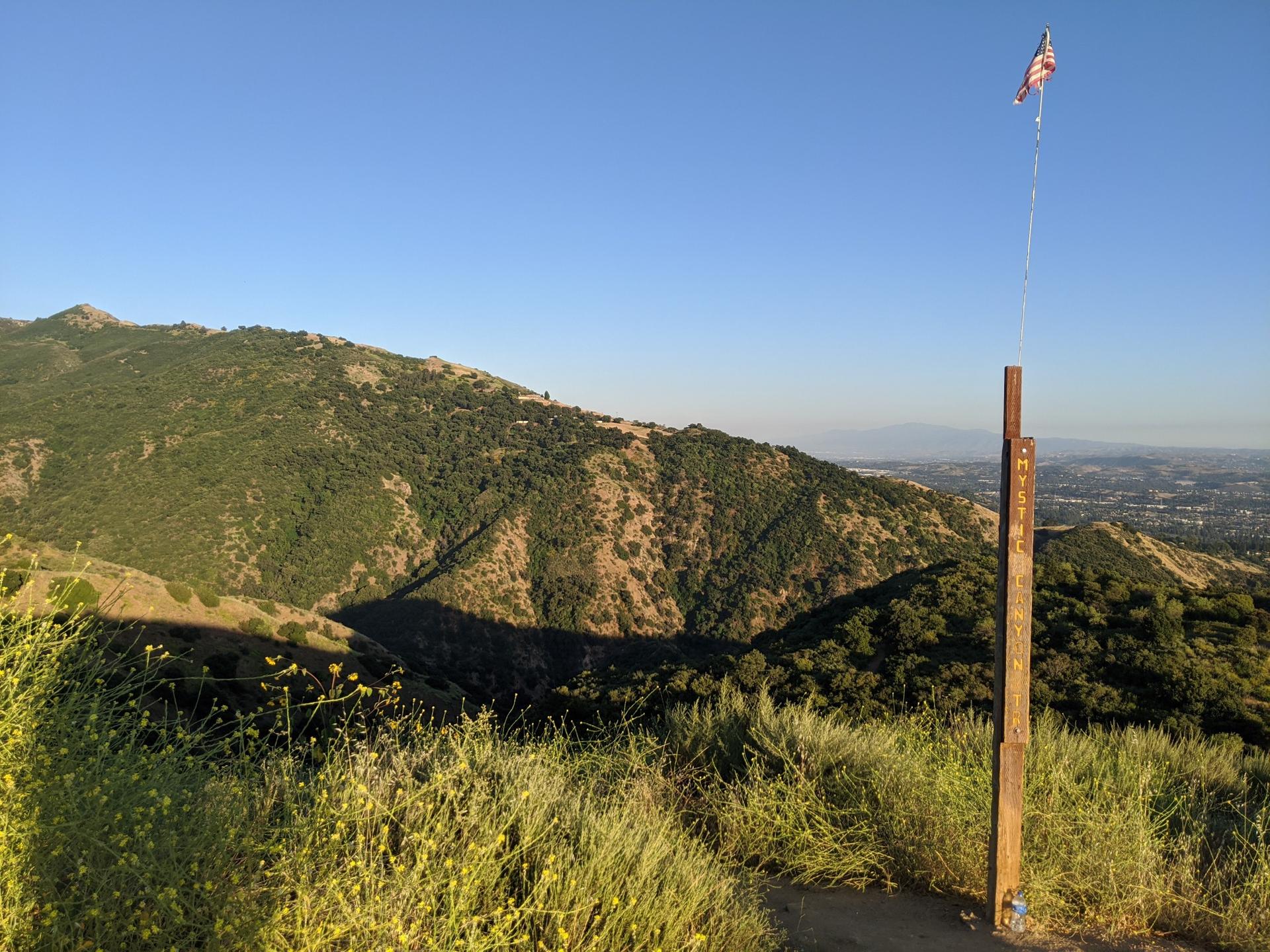 A flag on a wooden pole on a grassy mountain ridge under clear sky.