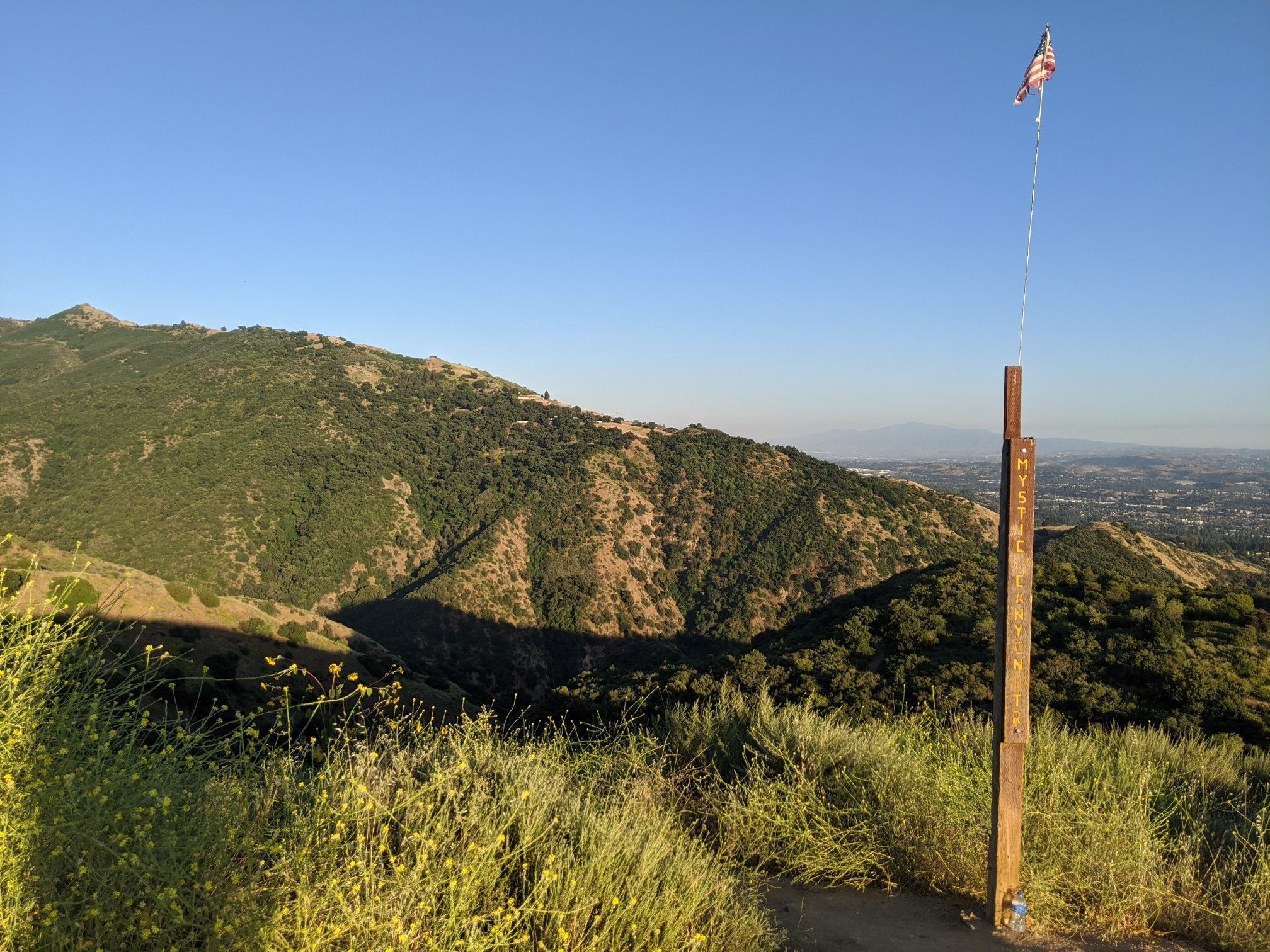 A flag on a wooden pole on a grassy mountain ridge under clear sky. - Glendora Mountain Loop