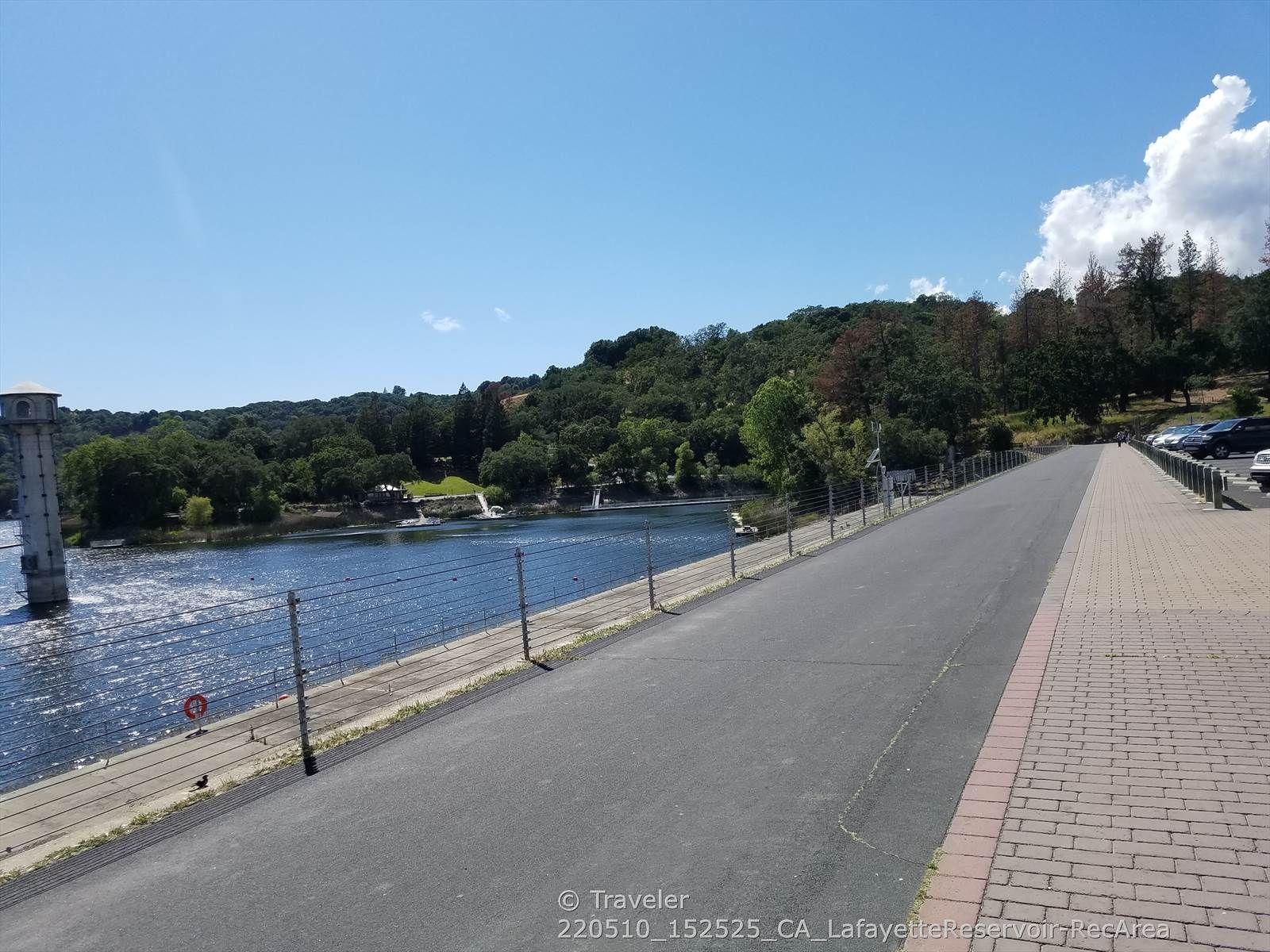 Paved path alongside a lake with a tower and green hills. - Rim Trail to Lafayette Viewpoint