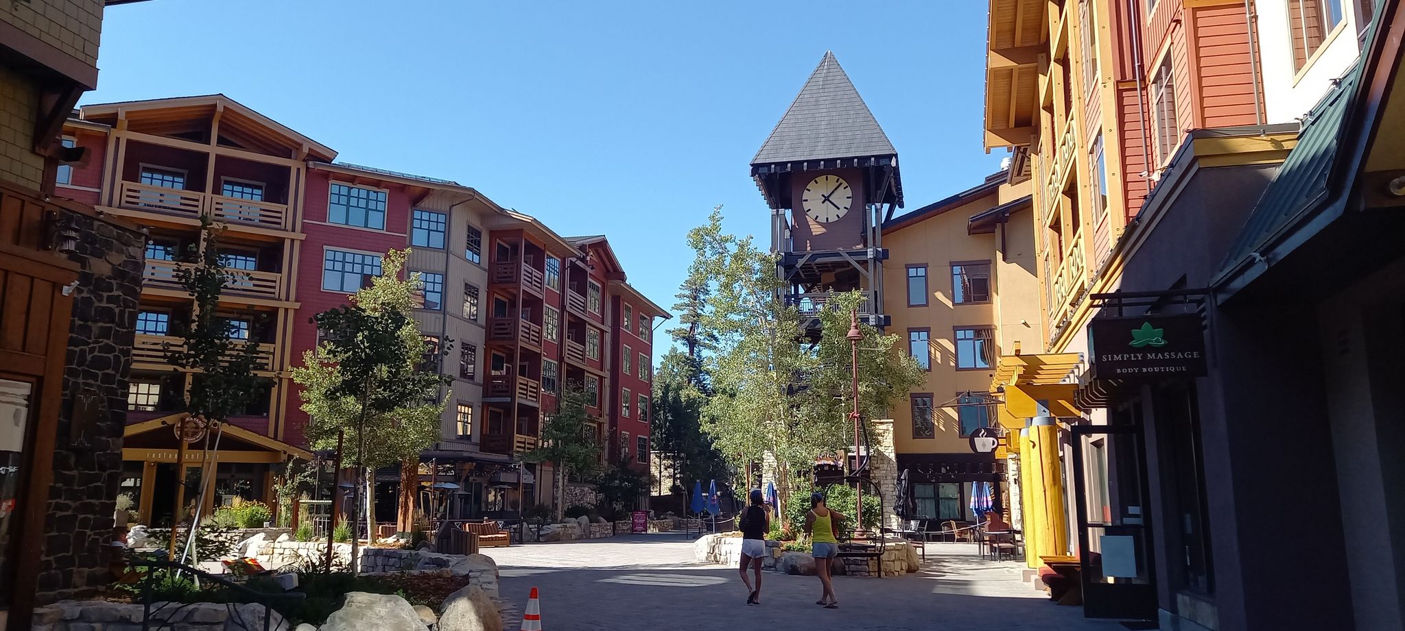 Sunny village square with multi-story buildings, a clock tower, and people walking. - Uptown and Downtown Trail Loop