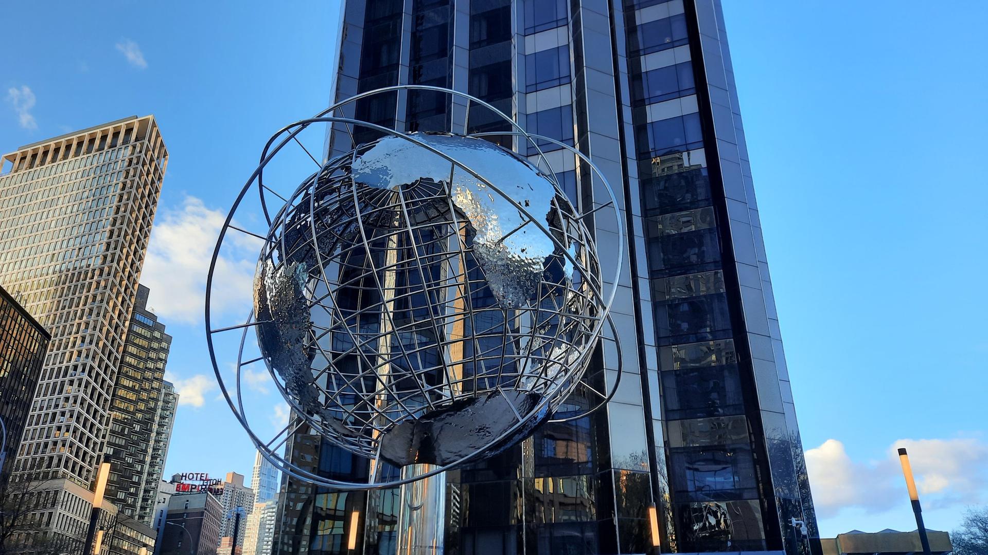 Large metallic globe sculpture in front of a tall glass building.