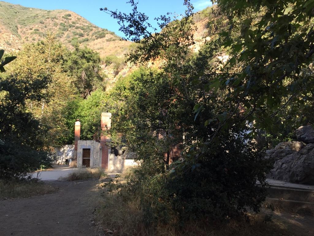 Old stone building ruins surrounded by trees in a sunlit valley.