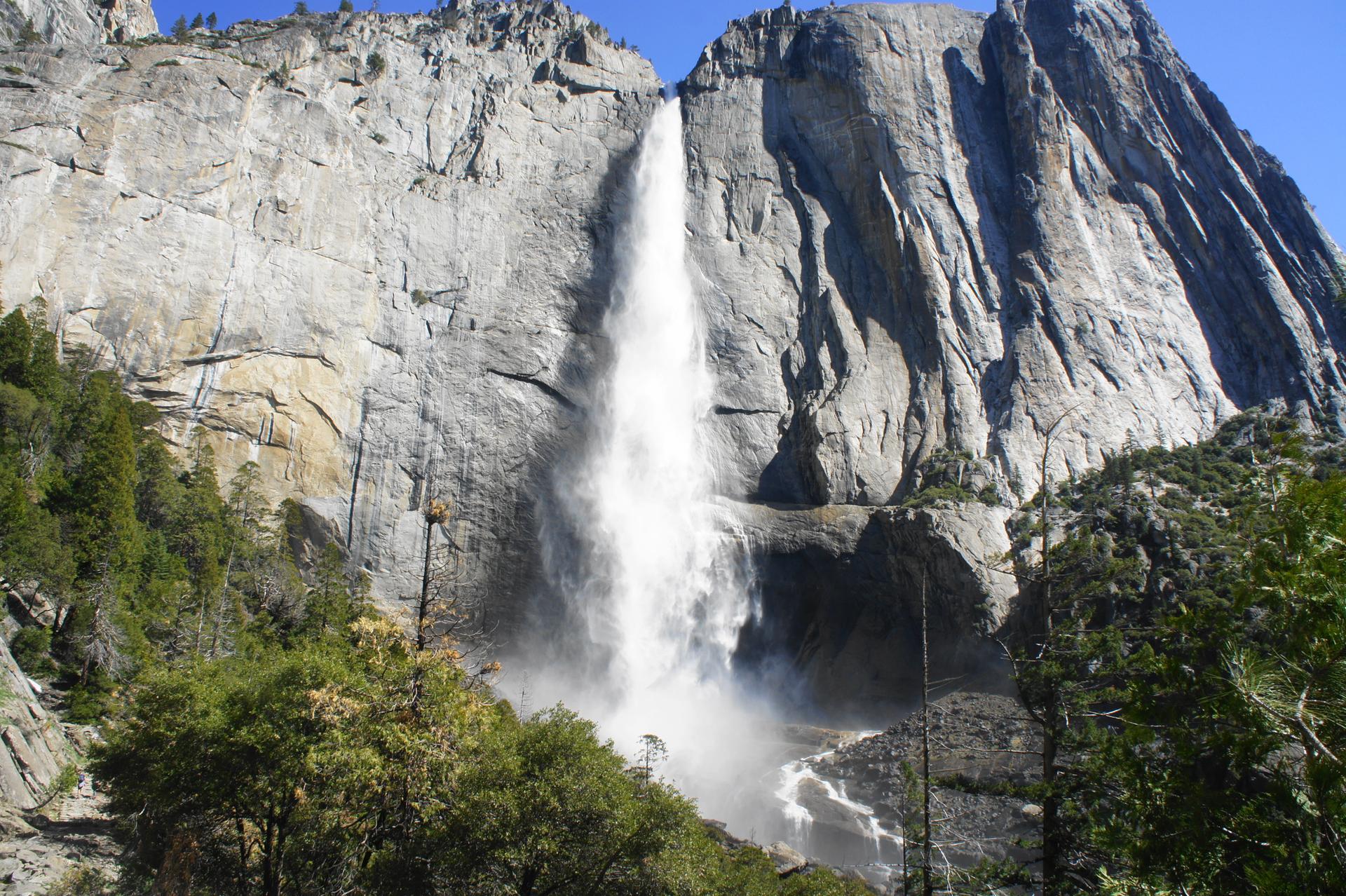 Powerful waterfall cascades down a massive rock cliff on a sunny day.