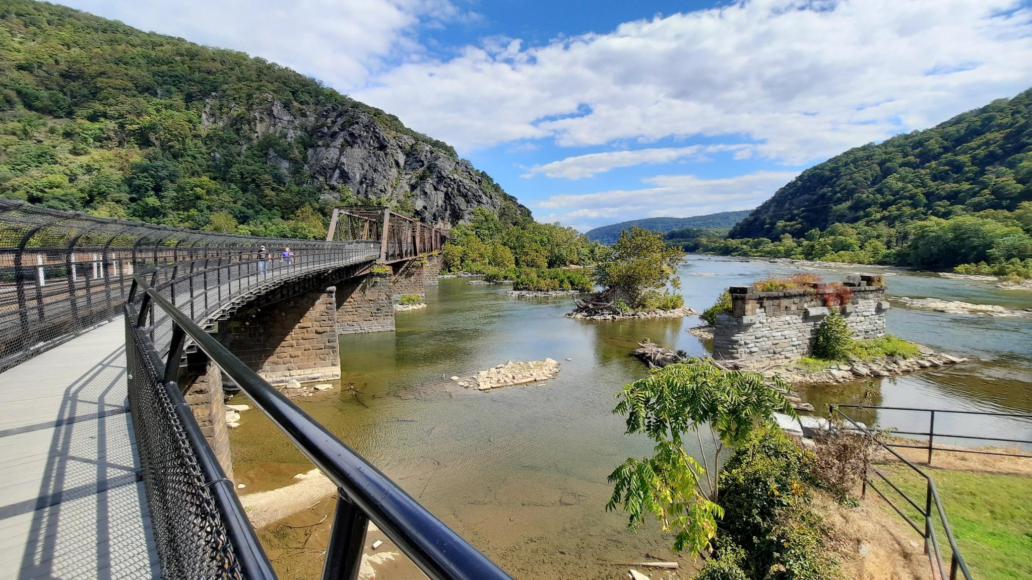 Bridge over river with stone ruins, green mountains, and blue sky.