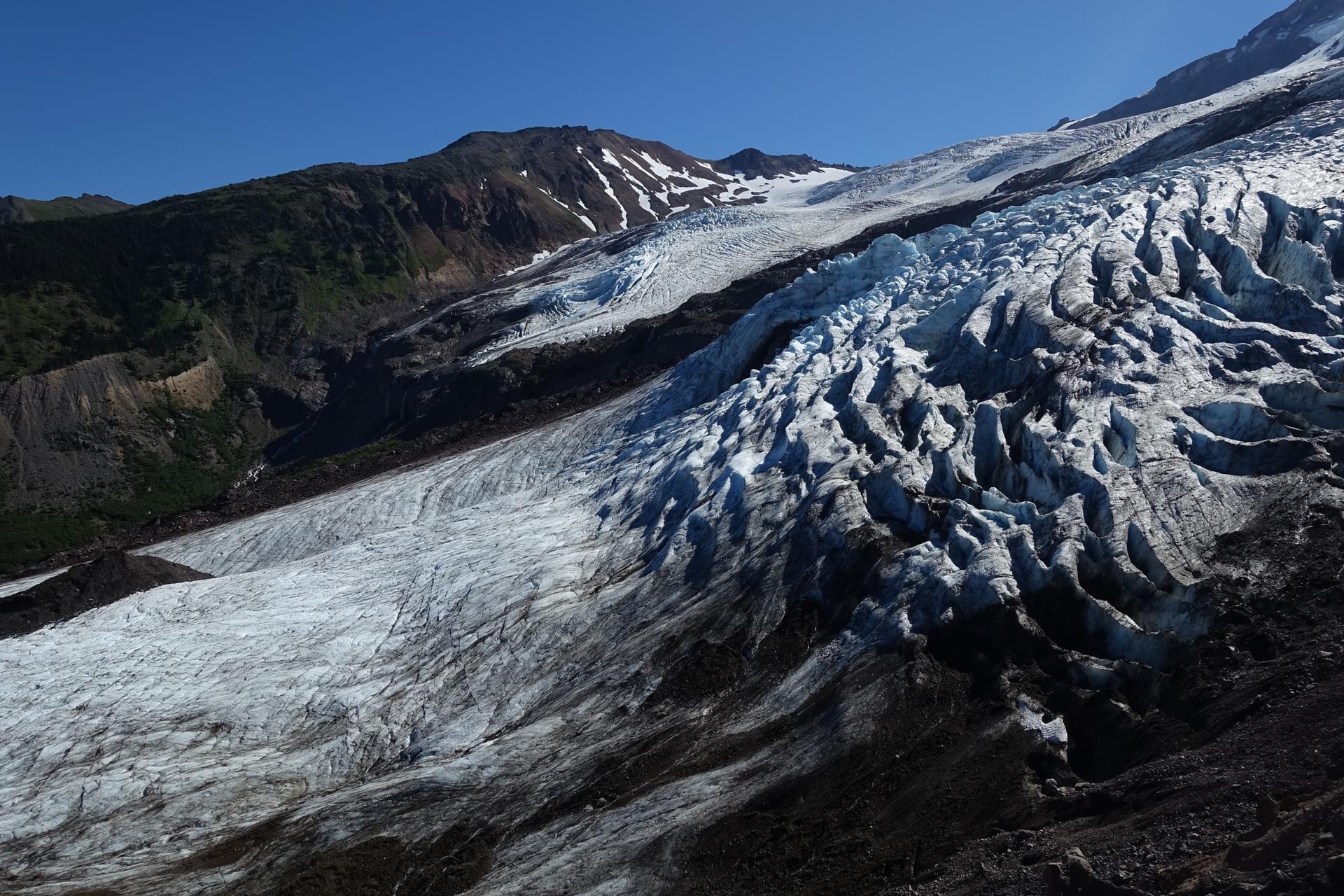 Vast, textured glacier flowing down a rocky mountain on a clear day.